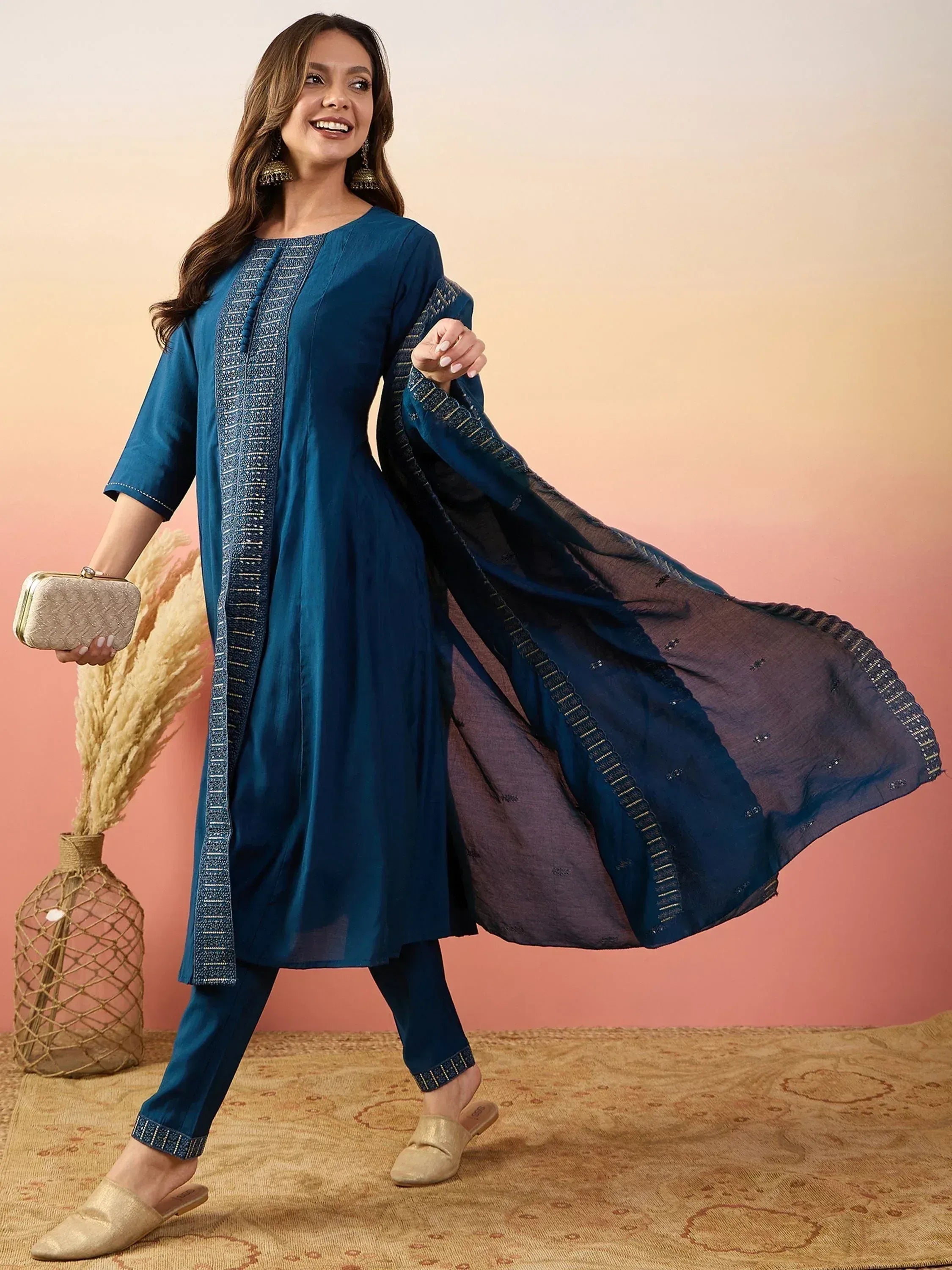 Woman in blue embroidered salwar kameez with matching dupatta, gold clutch, and ethnic jewelry