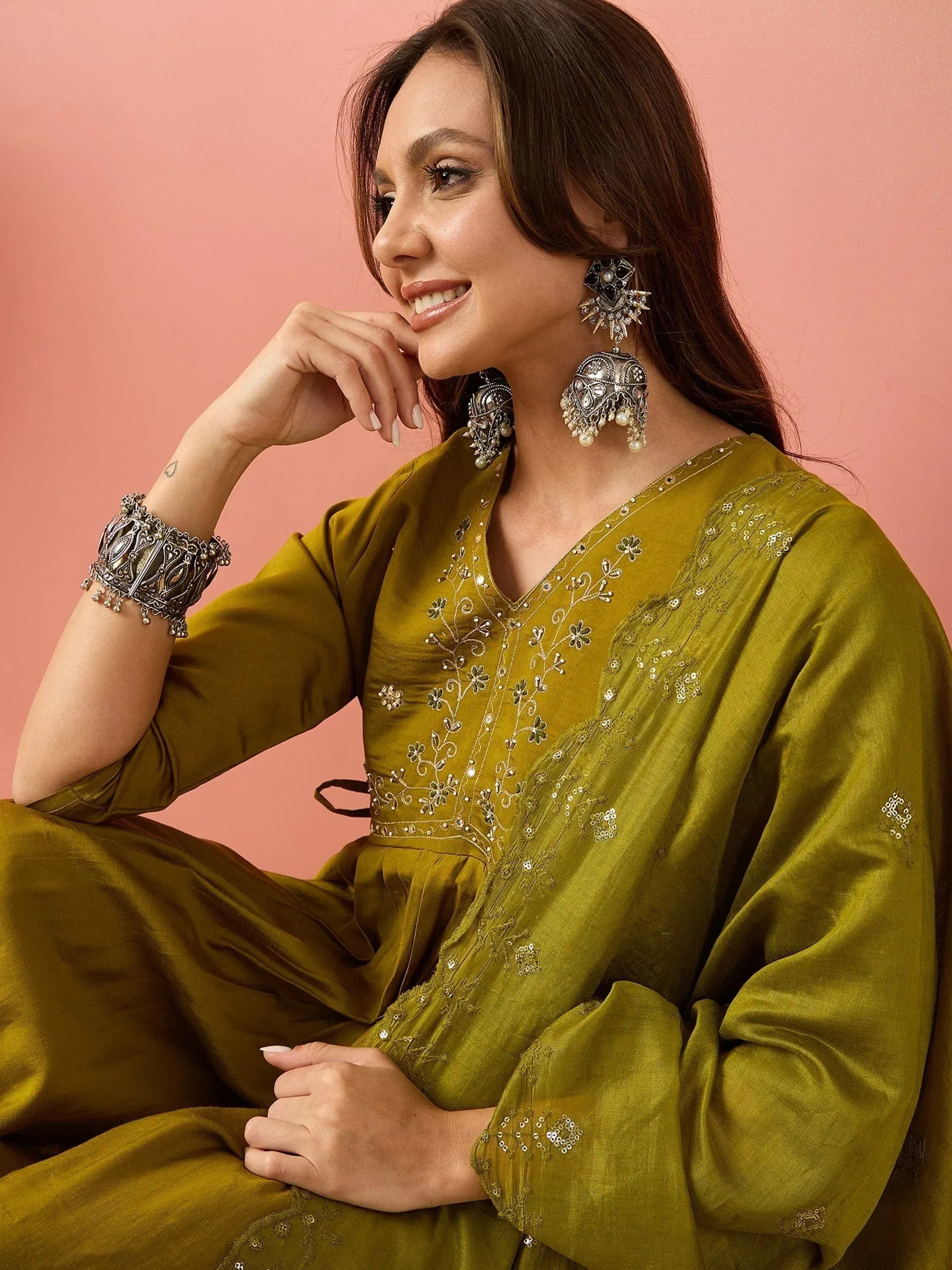 Olive green embroidered ethnic gown with floral detailing, paired with statement silver jewelry for festive occasions.