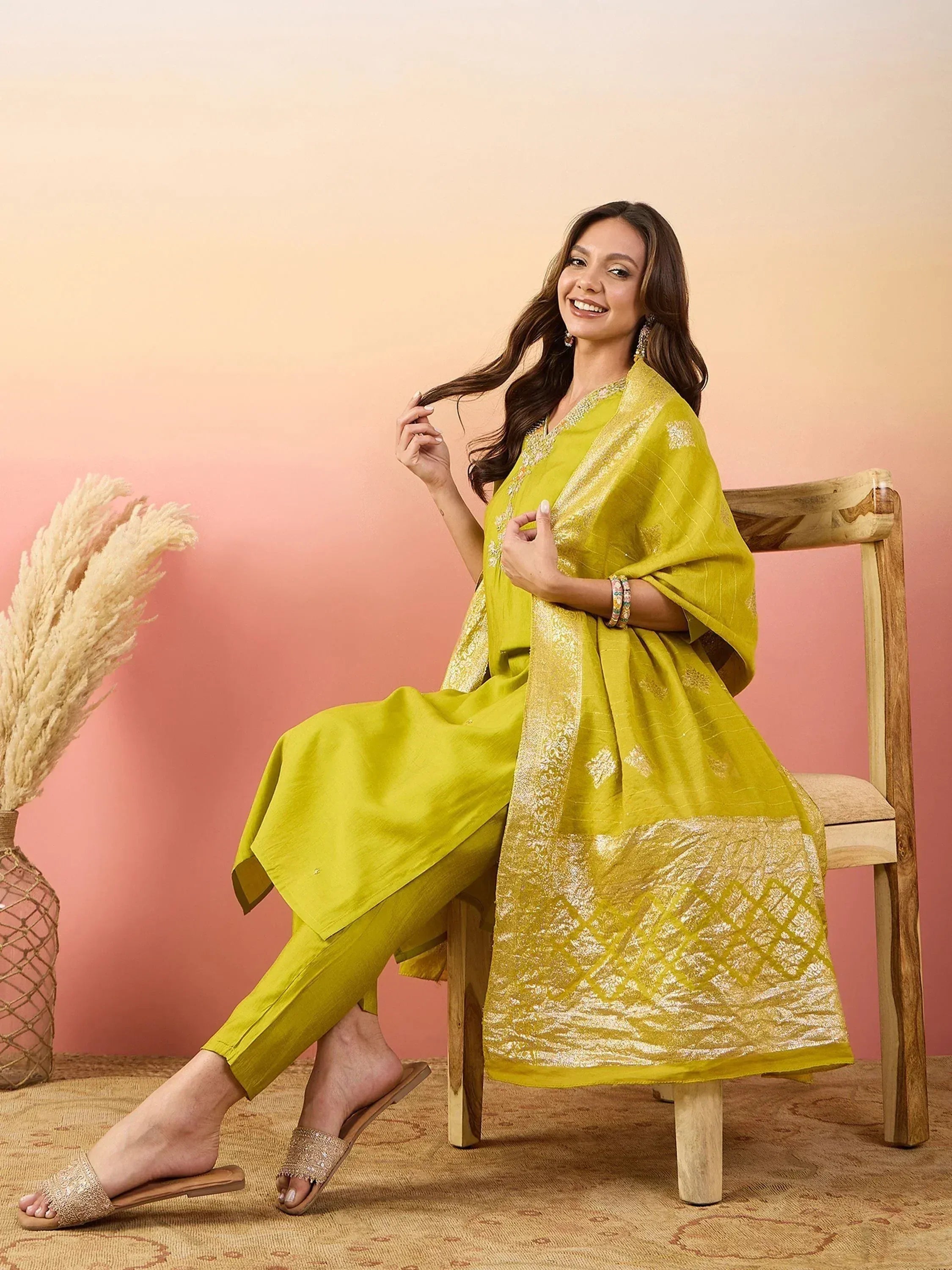 Woman in vibrant yellow ethnic salwar kameez with gold embroidery, seated on wooden chair, perfect for festive occasions