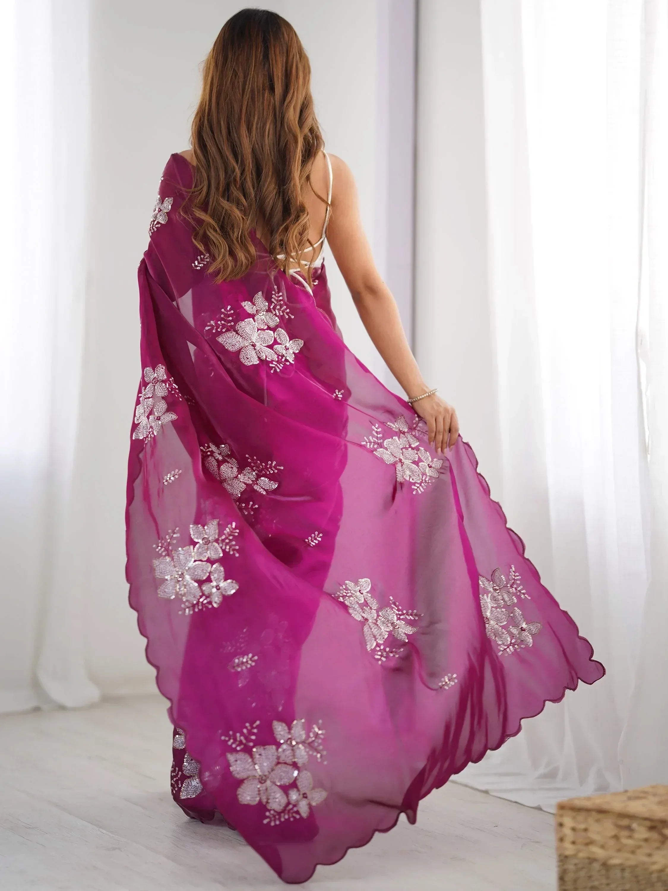 Woman in pink ethnic gown with floral embroidery, back view, sheer fabric, scalloped hem