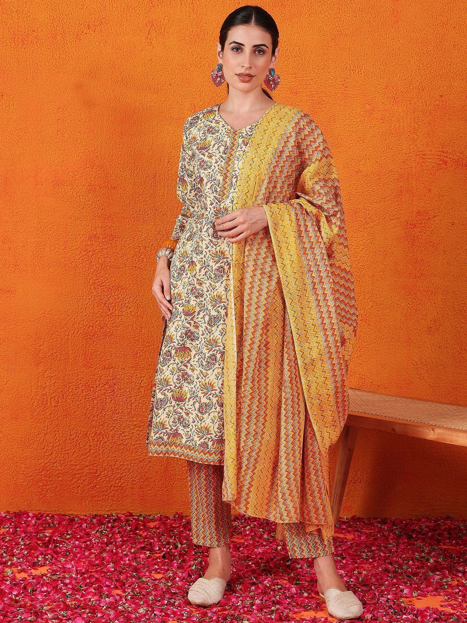 Woman in floral printed salwar kameez with yellow dupatta, standing on rose petals against orange wall