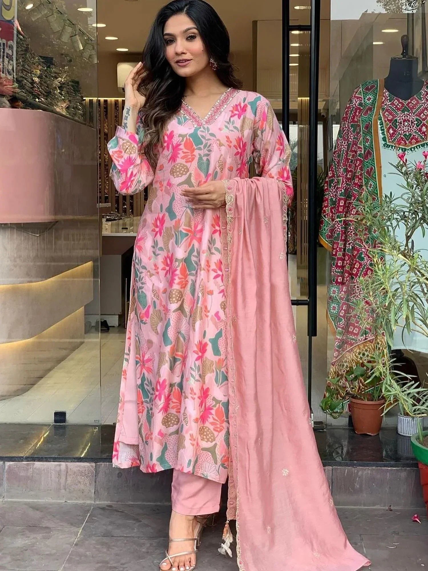 Woman wearing pink floral printed salwar kameez with matching dupatta, standing outside store