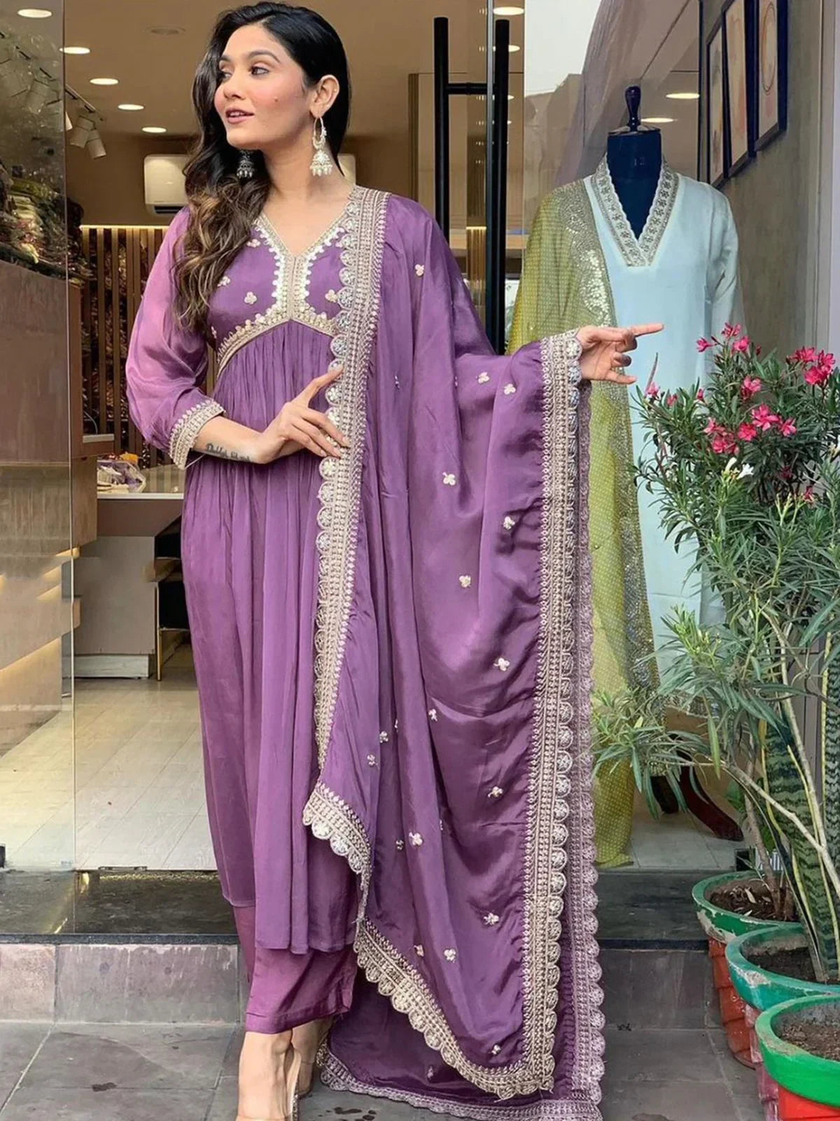 Woman wearing purple embroidered salwar kameez with dupatta, standing at boutique entrance