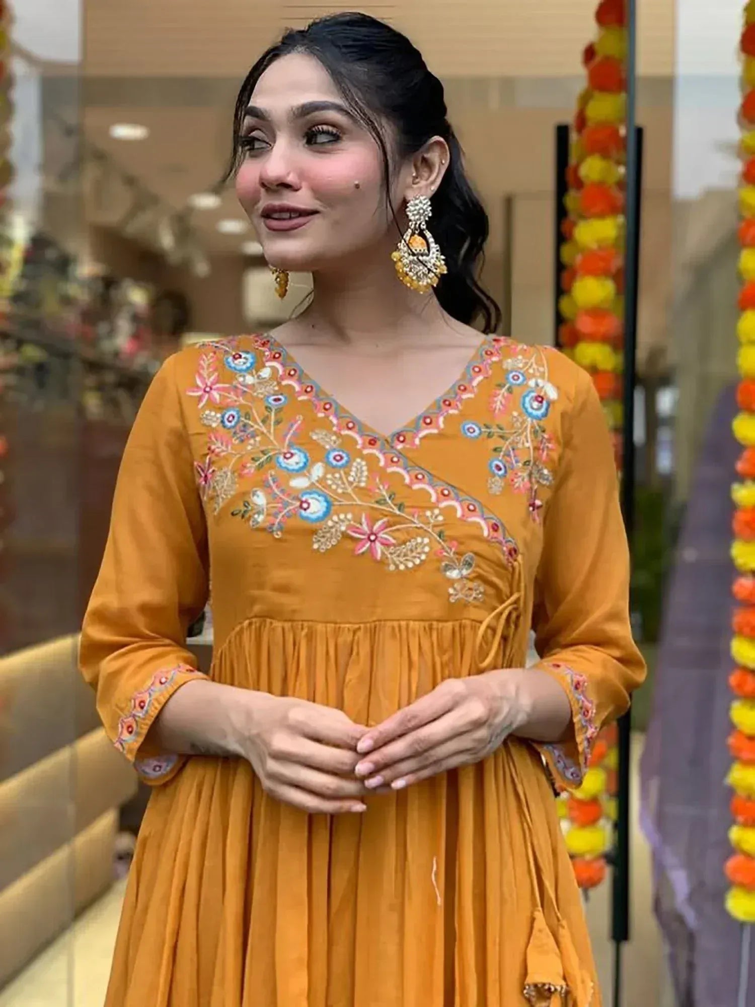 Woman in mustard yellow embroidered ethnic gown with floral detailing and statement earrings