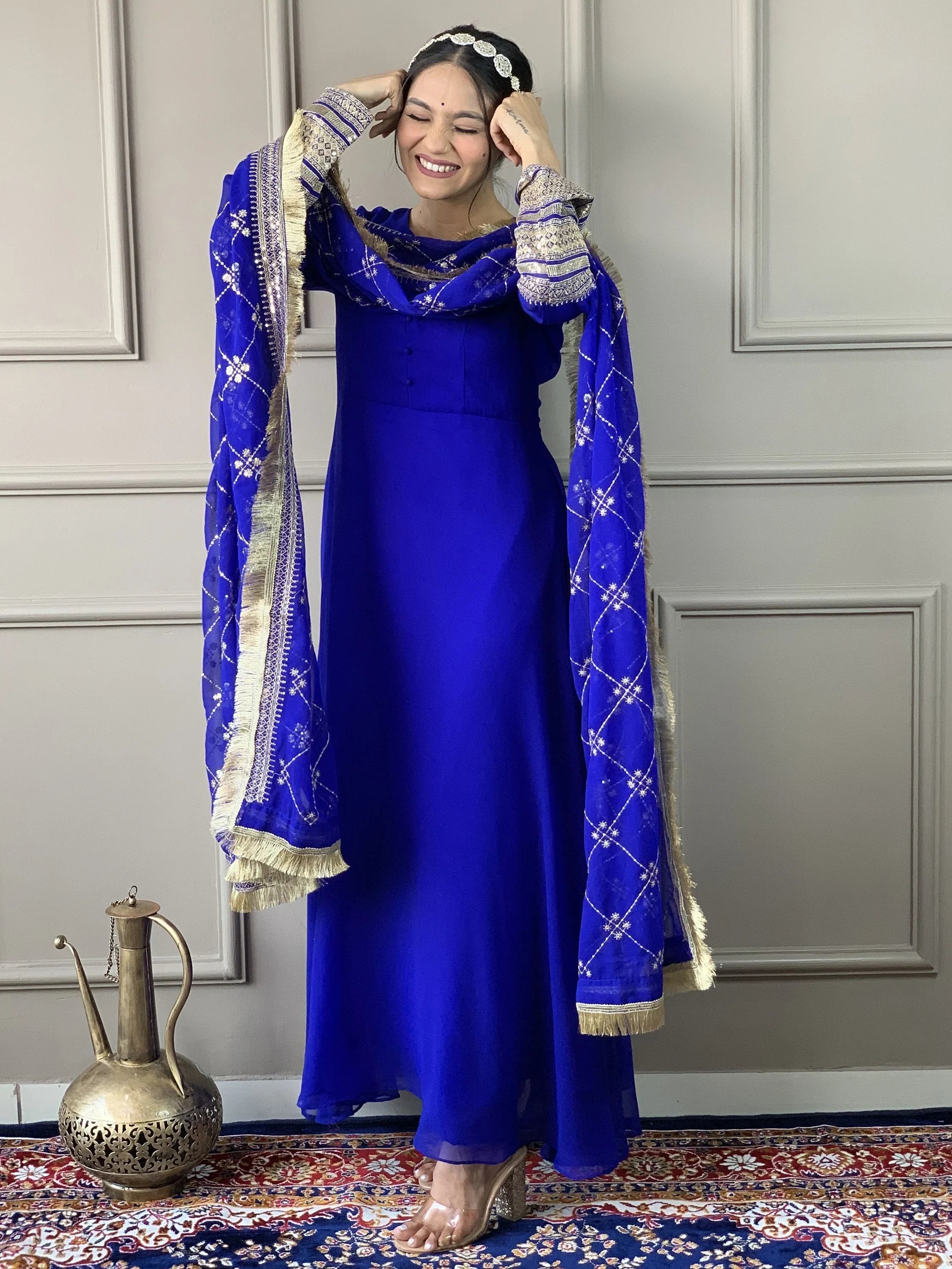 Woman in royal blue ethnic salwar kameez with embroidered dupatta, standing on patterned rug