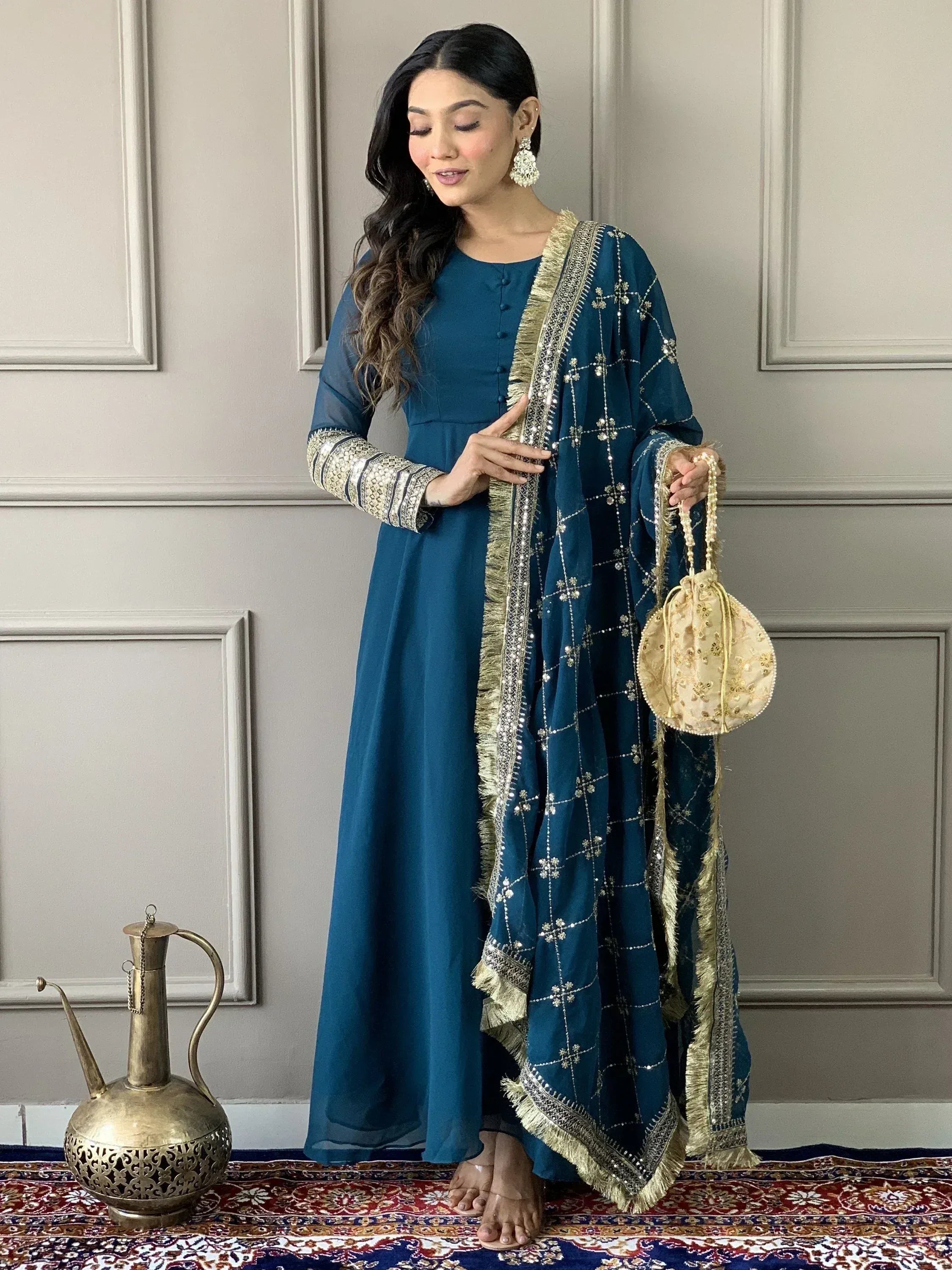 Teal ethnic gown with gold embroidery and matching dupatta, styled with ornate earrings and potli bag