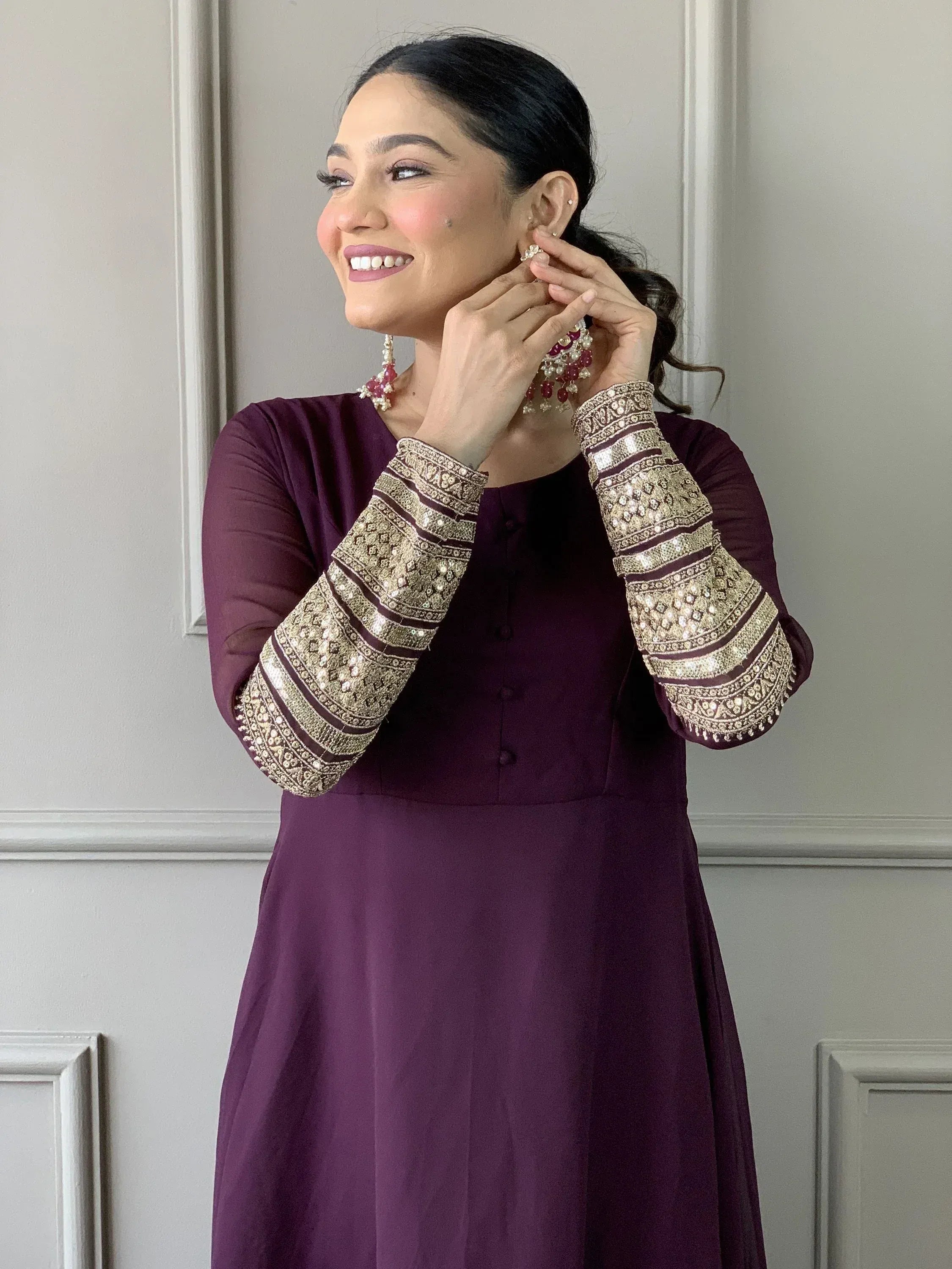 Woman in purple ethnic kurti with gold embroidered sleeves, wearing traditional jewelry, perfect for Indian occasions.