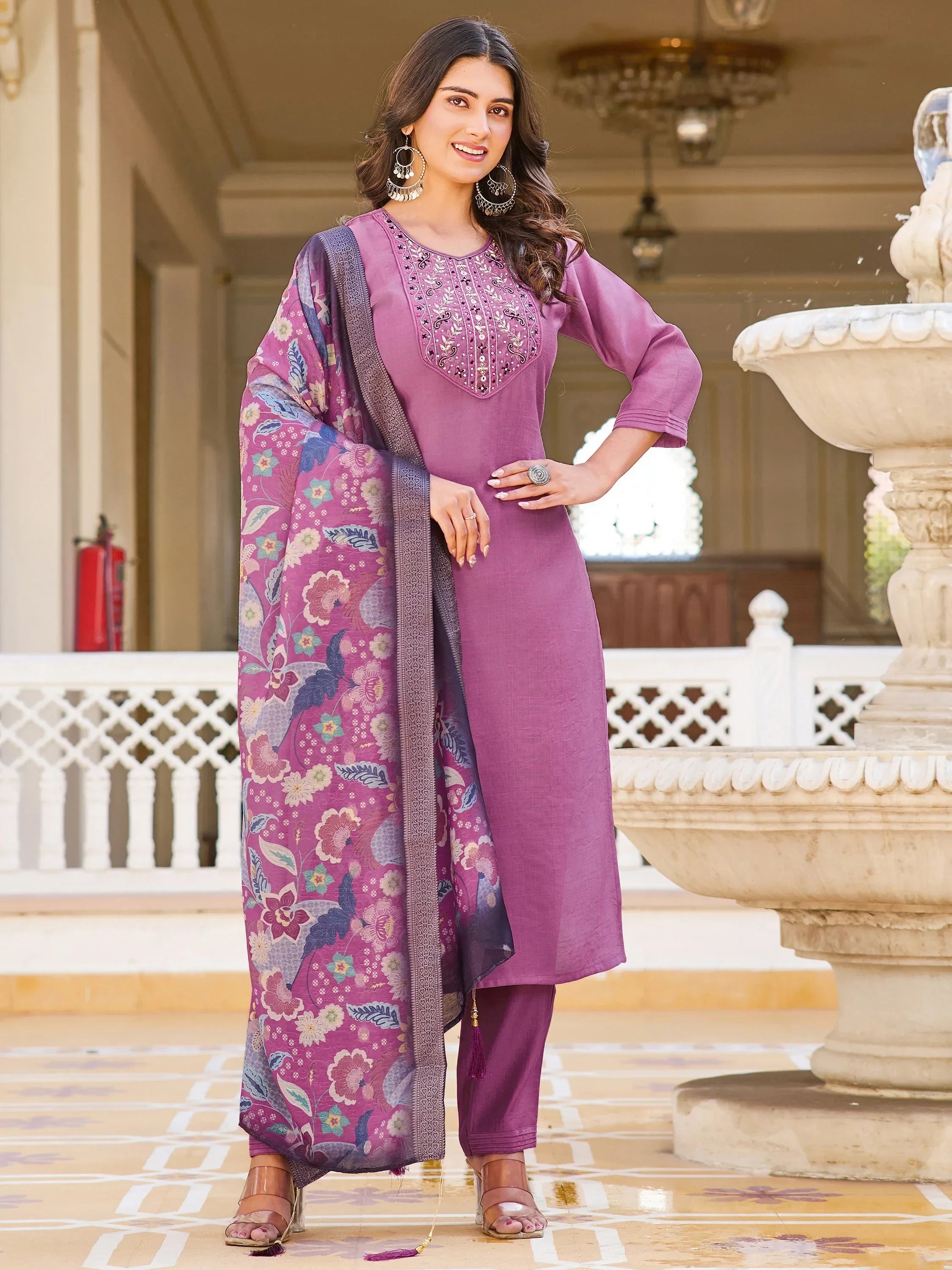 Woman in mauve embroidered salwar kameez with floral dupatta standing by fountain