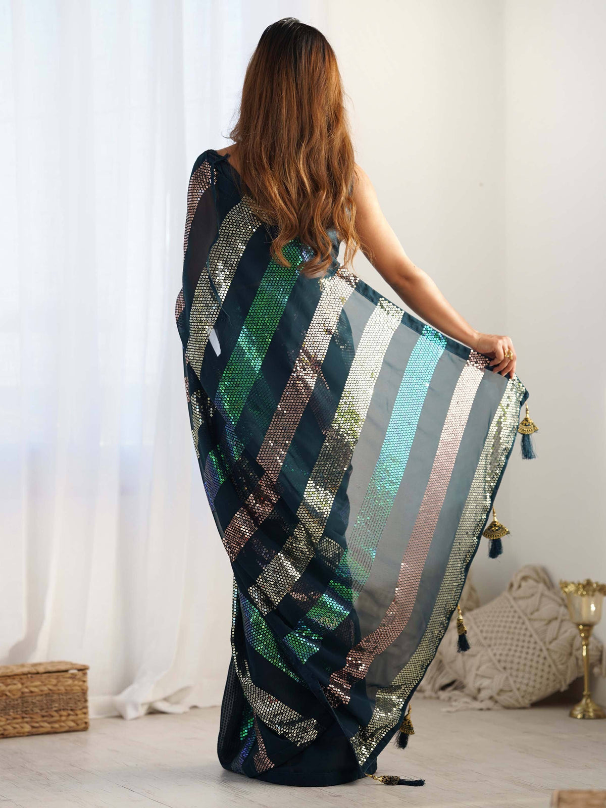 Woman in back view wearing a dark blue sequin saree with multicolor stripes and tassels, showcasing Indian ethnic wear.
