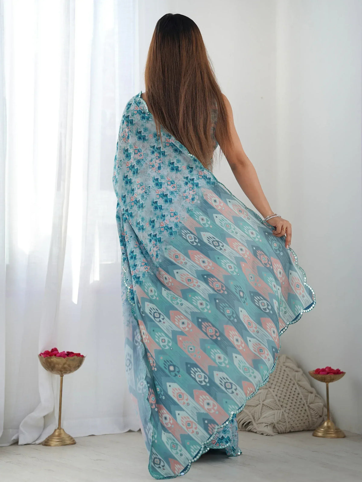 Woman in blue printed ethnic gown with sequin trim, back view near sheer curtains