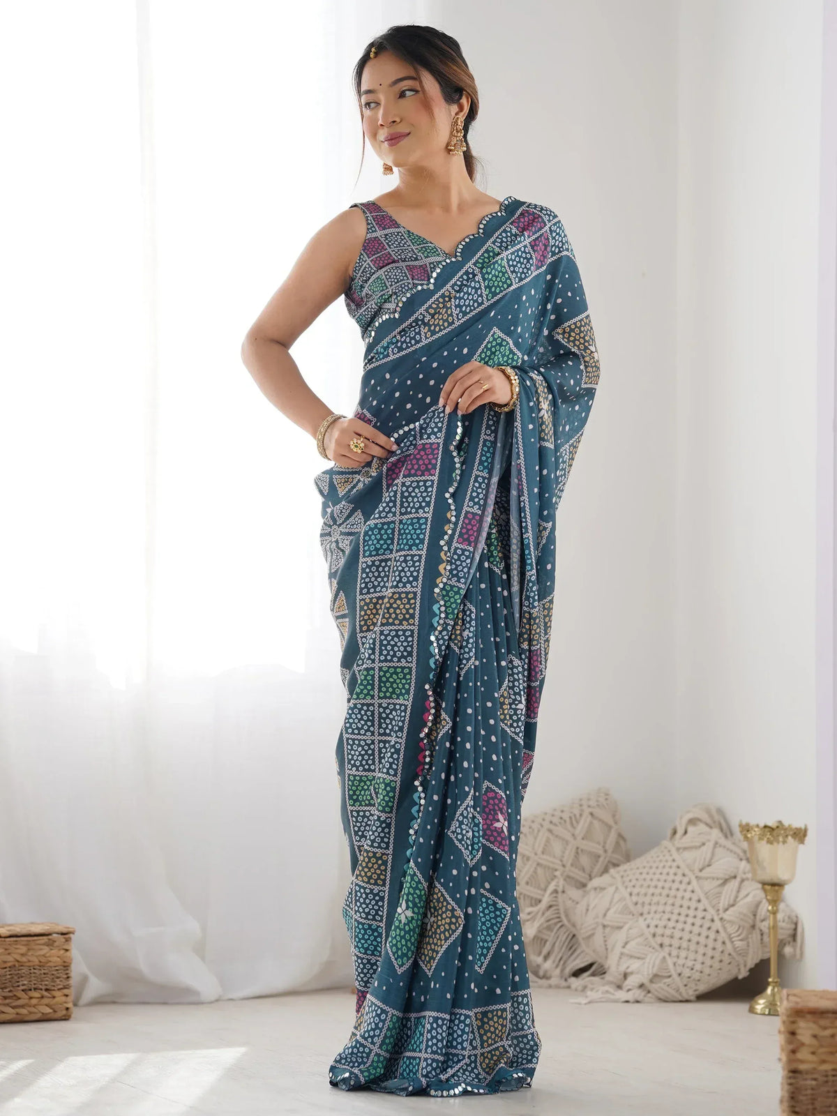 Teal printed saree with geometric patterns and mirror work, styled with gold jewelry for ethnic wear