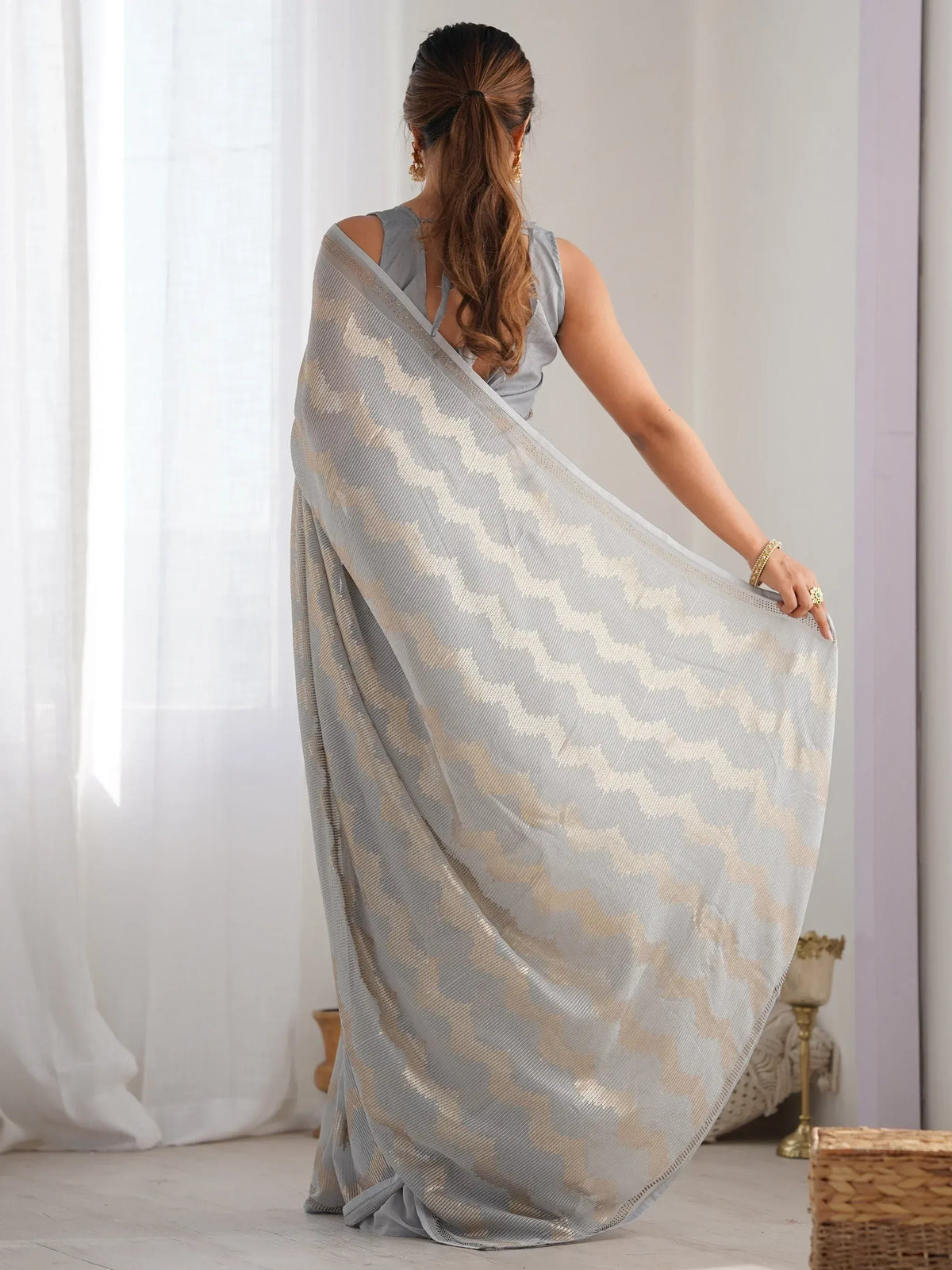 Grey and gold patterned saree with sheer fabric, styled with sleeveless blouse, perfect for ethnic occasions