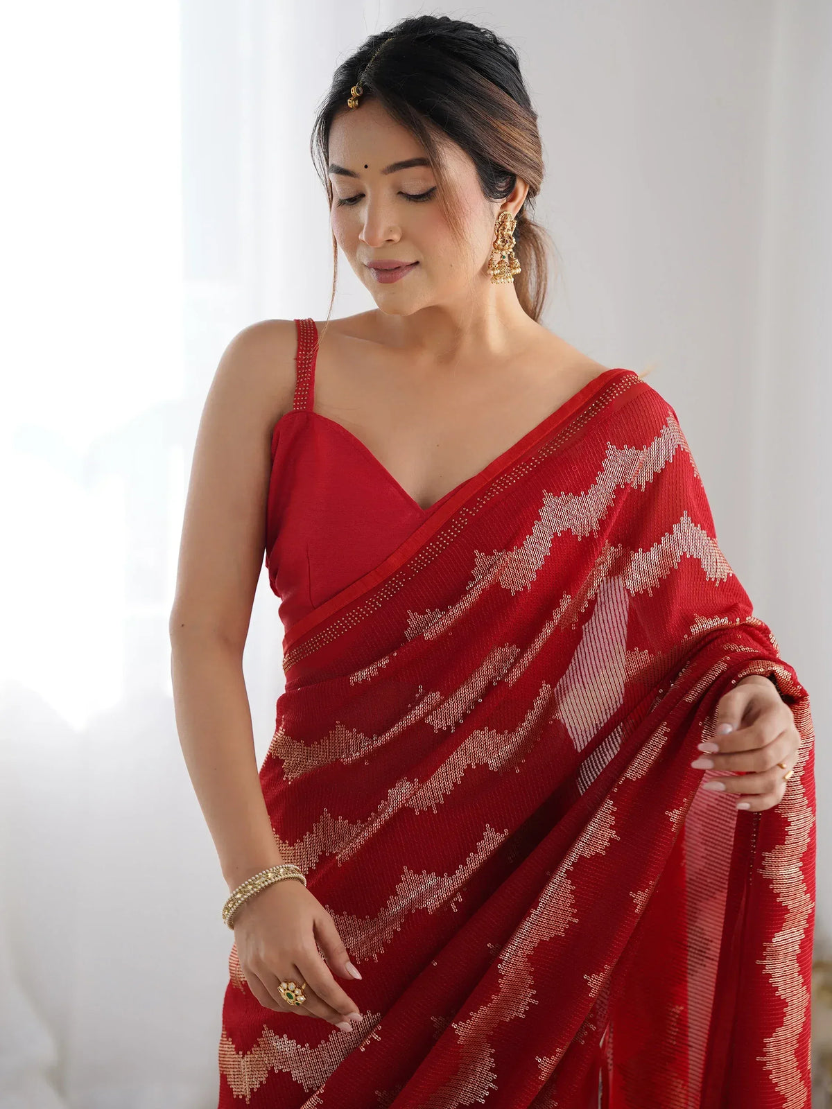 Red ethnic saree with gold geometric pattern, paired with spaghetti blouse and traditional jewelry