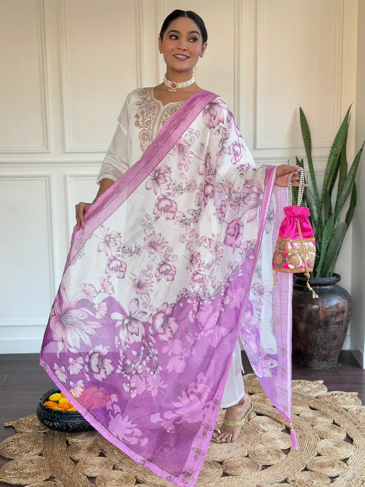 Woman in white embroidered kurta with pink floral dupatta, holding pink potli bag, ethnic wear outfit