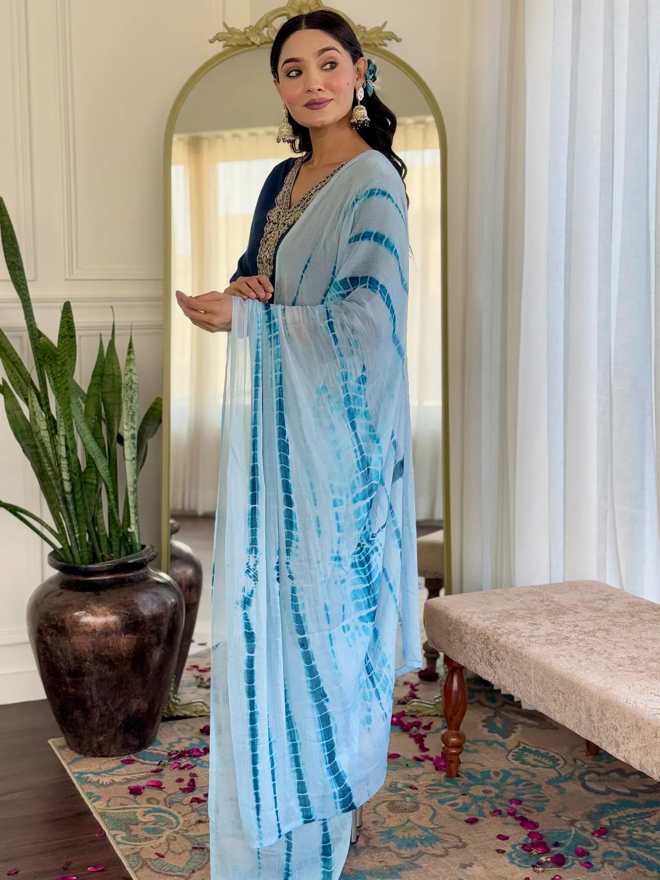 Woman in blue tie-dye ethnic kurta with gold embroidery, styled with statement earrings and floral hair accessory.