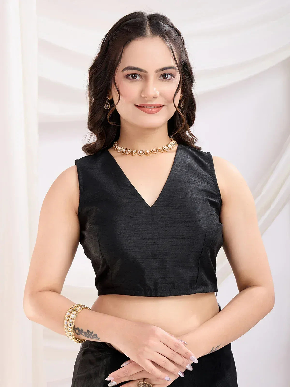 Black sleeveless V-neck crop top for ethnic wear, paired with gold jewelry and matching bottom.