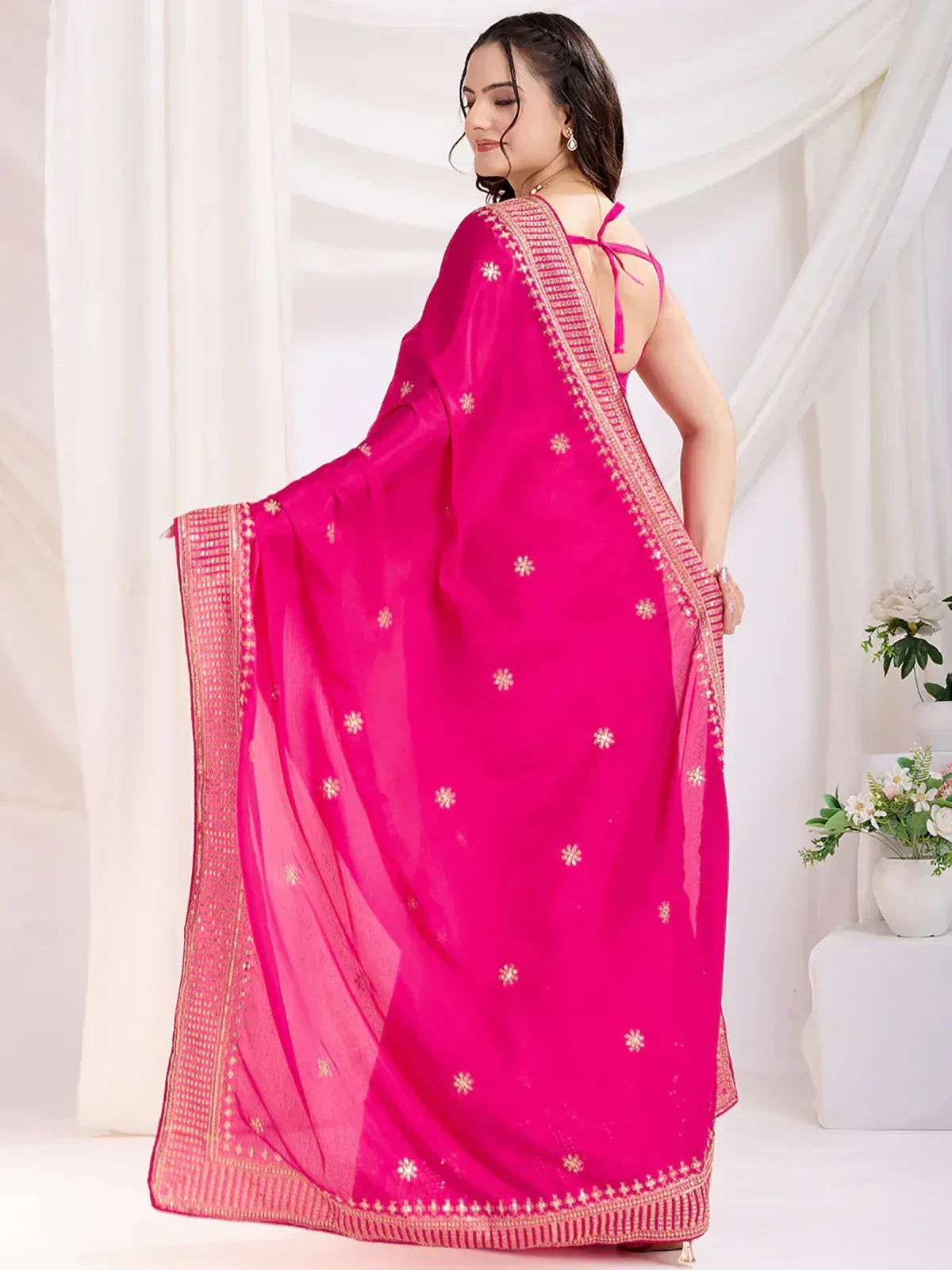 Vibrant pink ethnic saree with gold floral embroidery and border, styled with back-tie blouse for festive occasions
