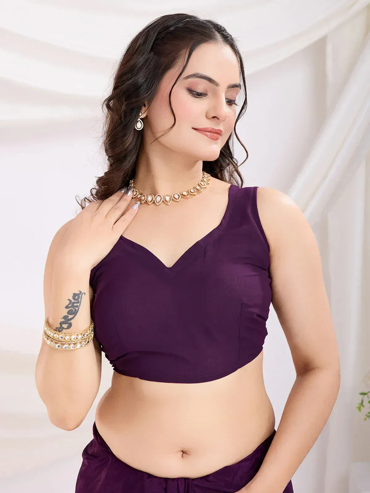 Purple V-neck sleeveless blouse with matching ethnic wear, styled with gold jewelry for Indian occasions