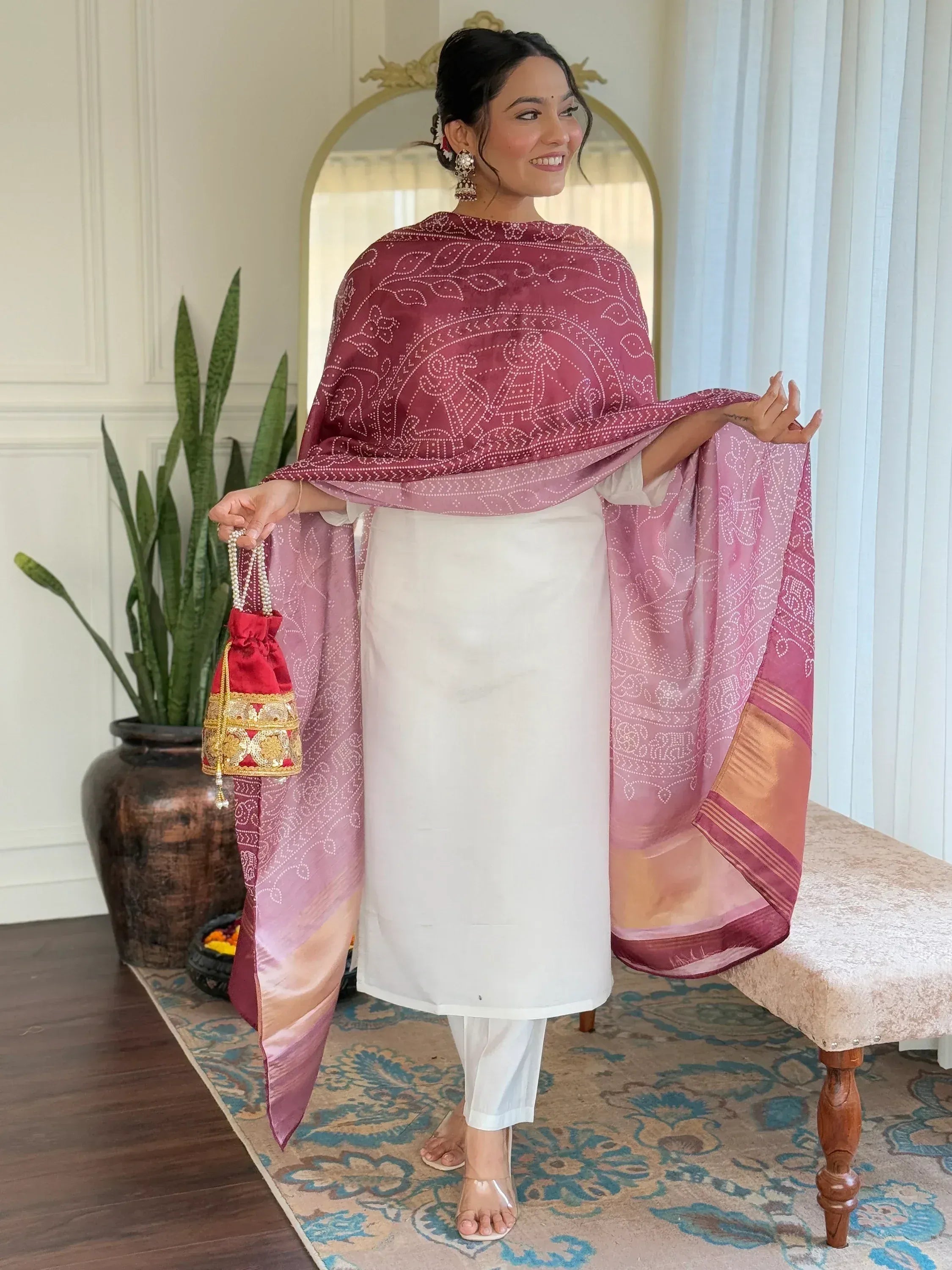Woman in white kurta with maroon bandhani dupatta, holding red potli bag, ethnic Indian wear