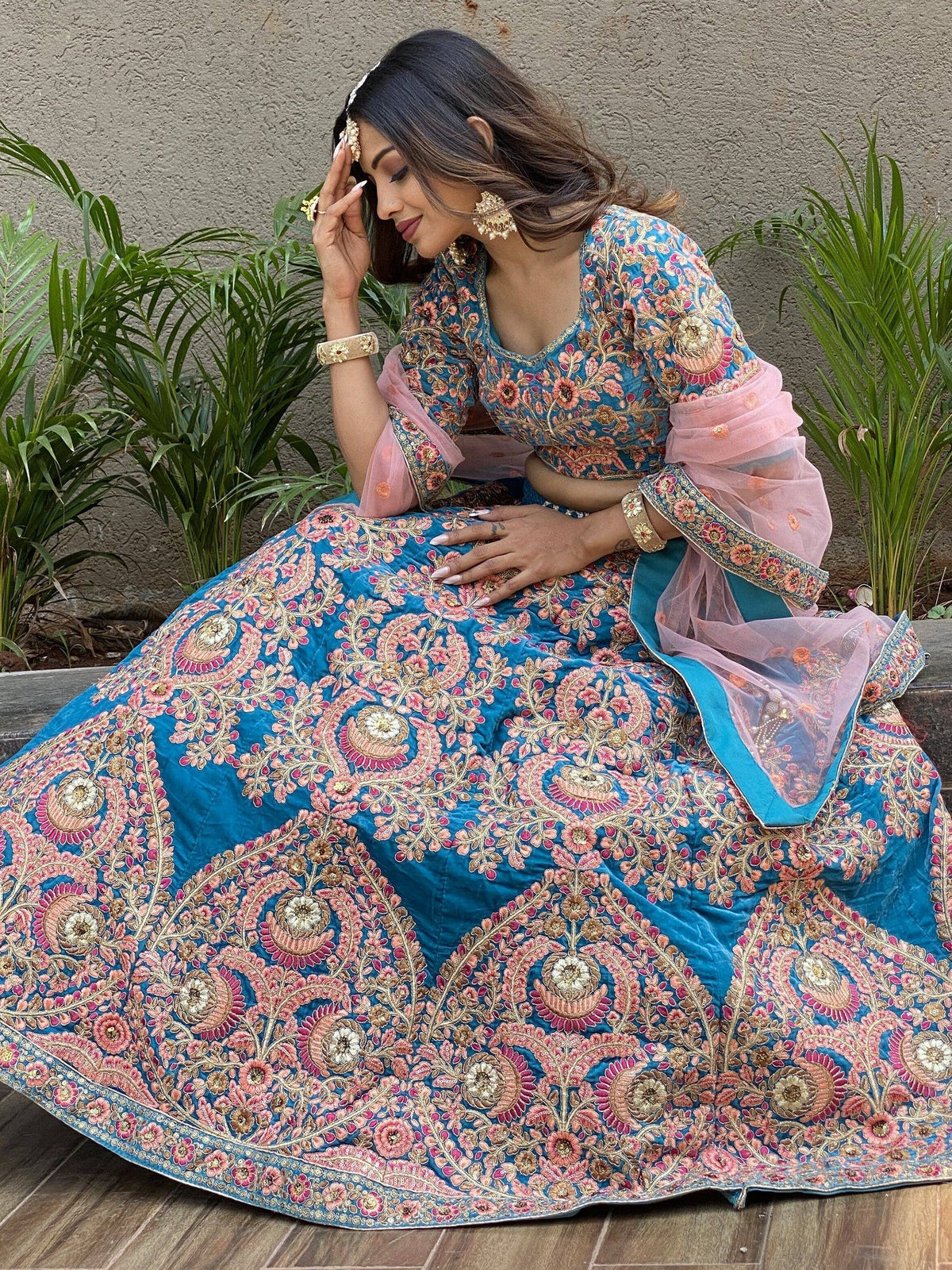 Blue velvet lehenga choli with pink floral embroidery and sheer sleeves, perfect for Indian weddings or festive occasions.