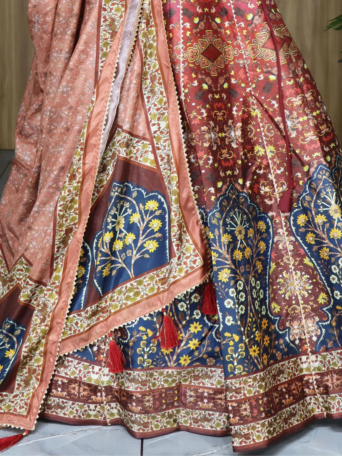 Designer lehenga choli with intricate floral and paisley prints in red, blue, and peach, featuring tassels and border details.