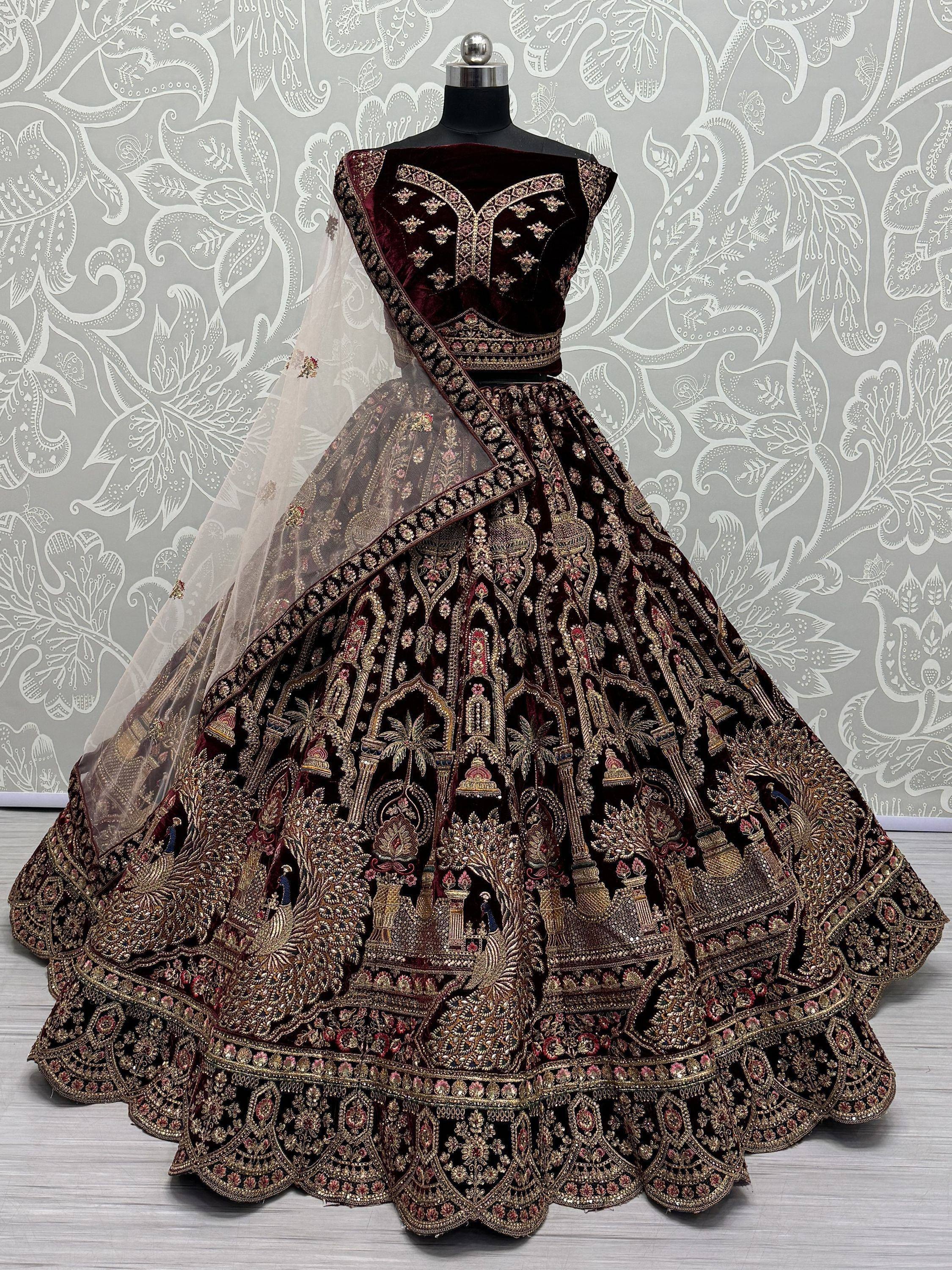 Luxury maroon velvet lehenga choli with heavy gold embroidery and sheer dupatta, perfect for Indian weddings.