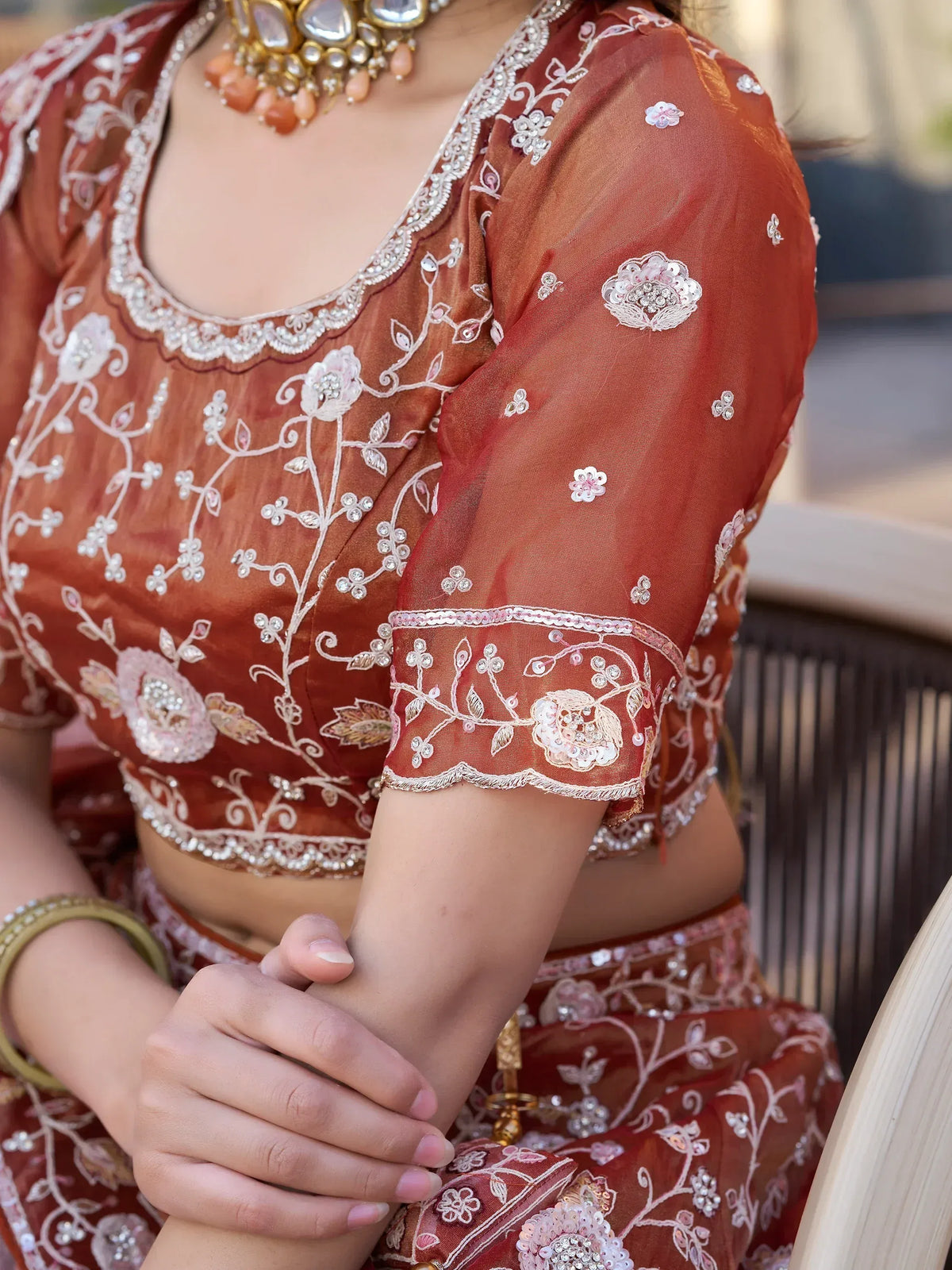 Rust orange embroidered lehenga choli with floral motifs and pearl detailing, paired with traditional jewelry