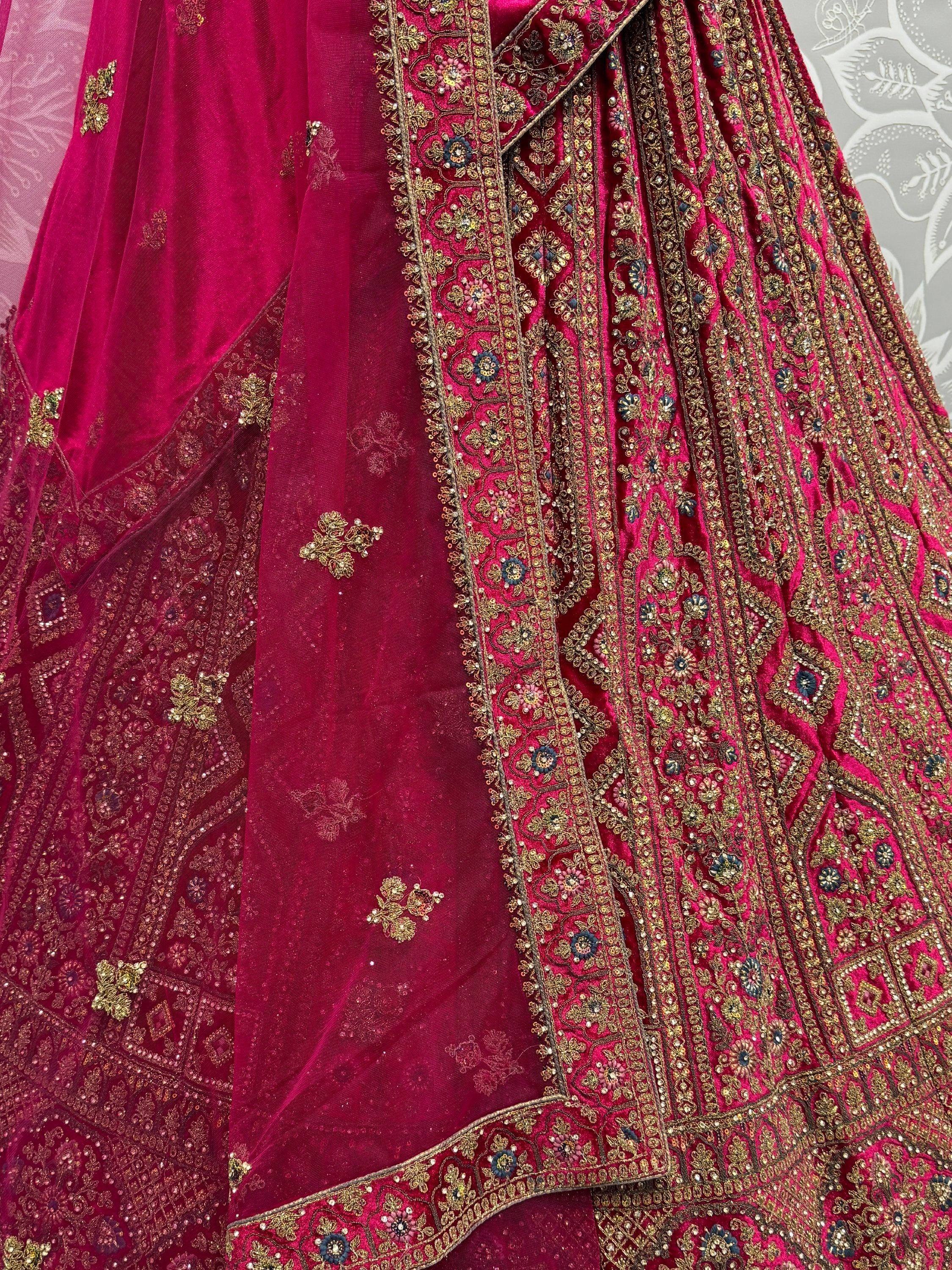 Luxury maroon velvet lehenga choli with heavy gold embroidery and floral motifs, perfect for Indian weddings.