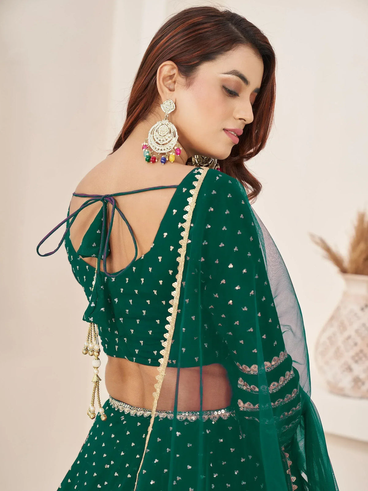 Emerald green designer lehenga choli with back tie-up, sequin work, and colorful jhumka earrings