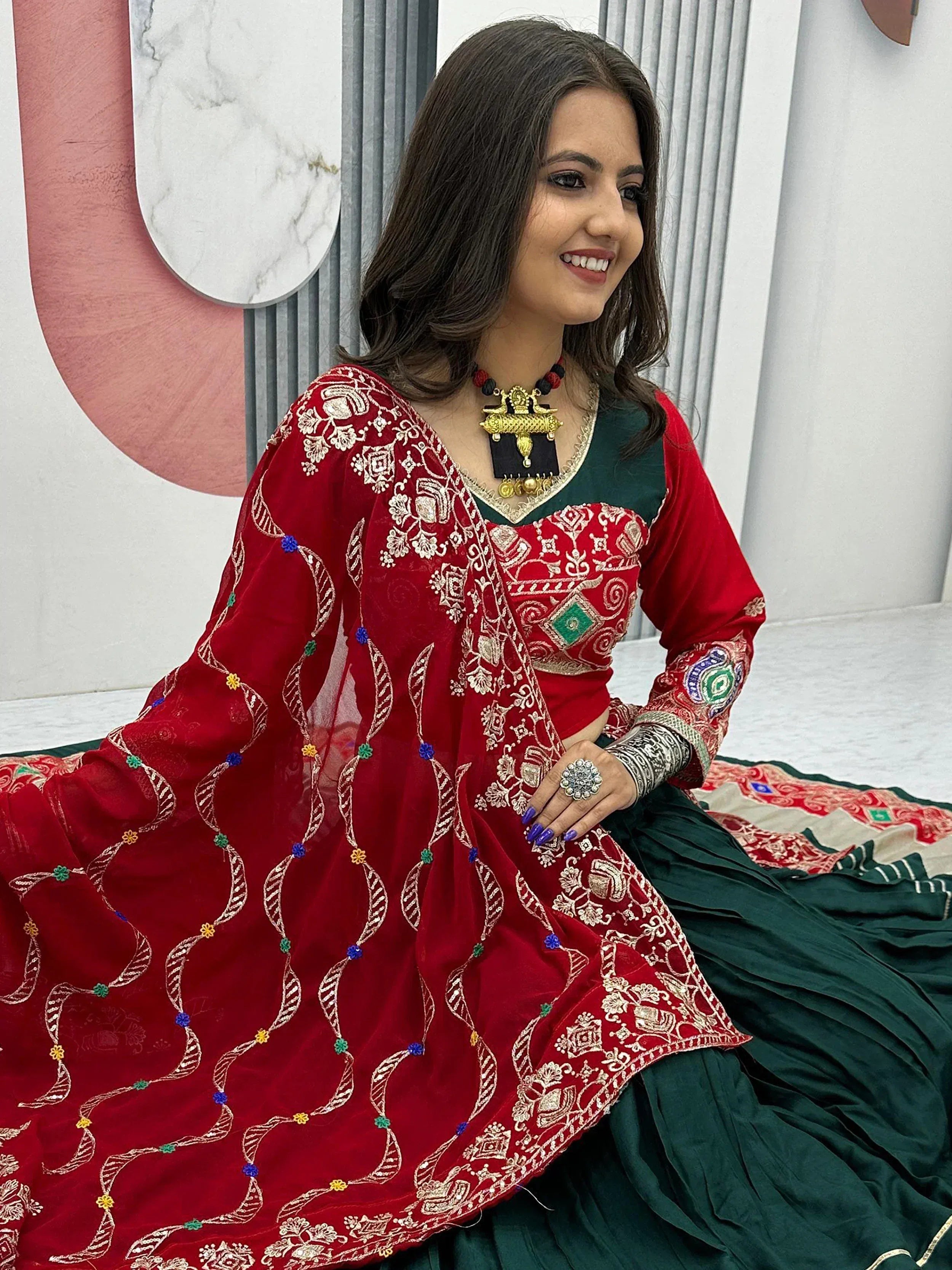 Red and green embroidered ethnic lehenga choli with gold detailing and traditional jewelry
