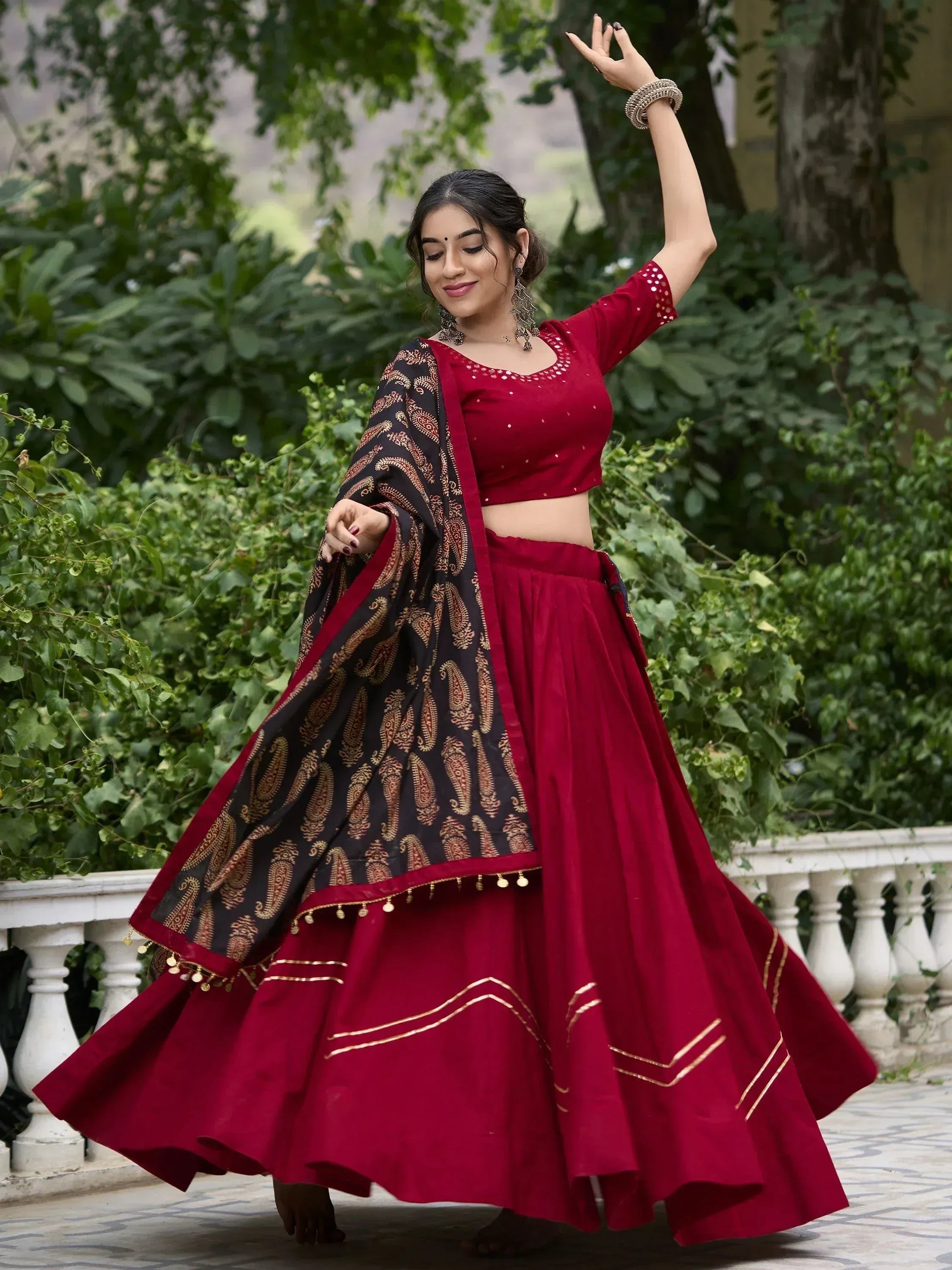 Woman in maroon lehenga choli with black paisley dupatta, dancing outdoors
