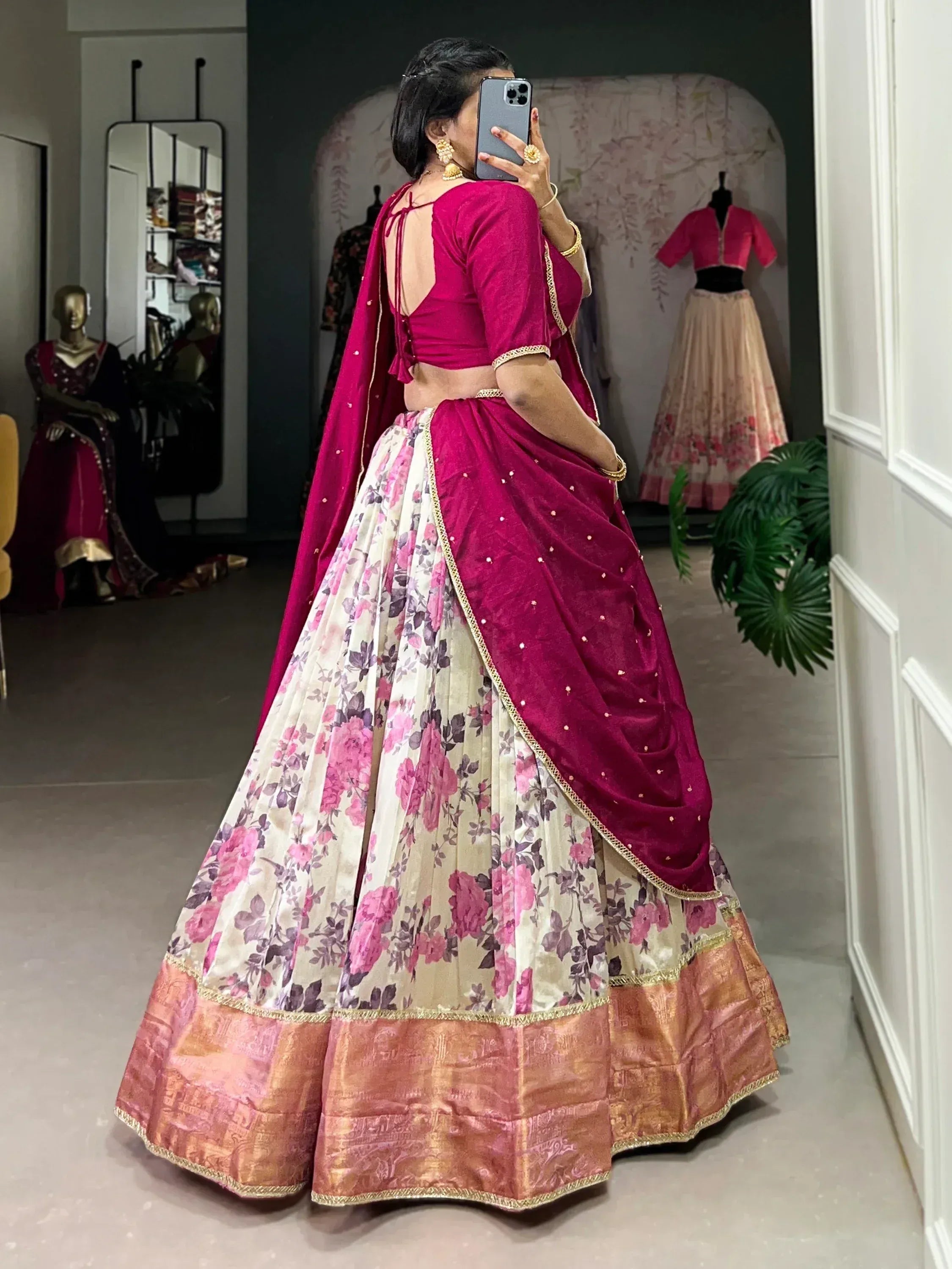Woman in pink floral lehenga choli with gold trim, taking mirror selfie in boutique