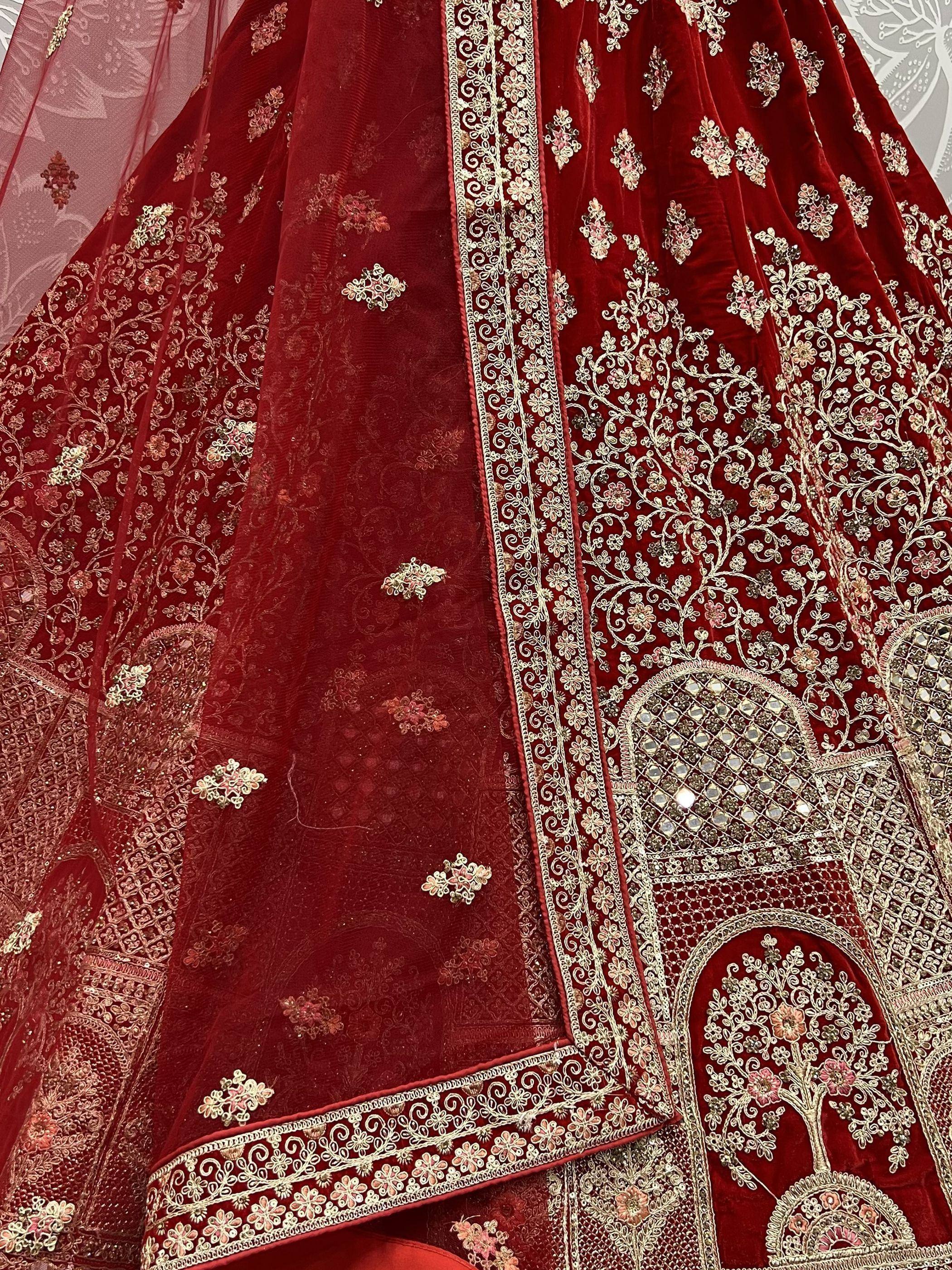 Red velvet lehenga choli with intricate gold embroidery and mirror work, perfect for Indian weddings.