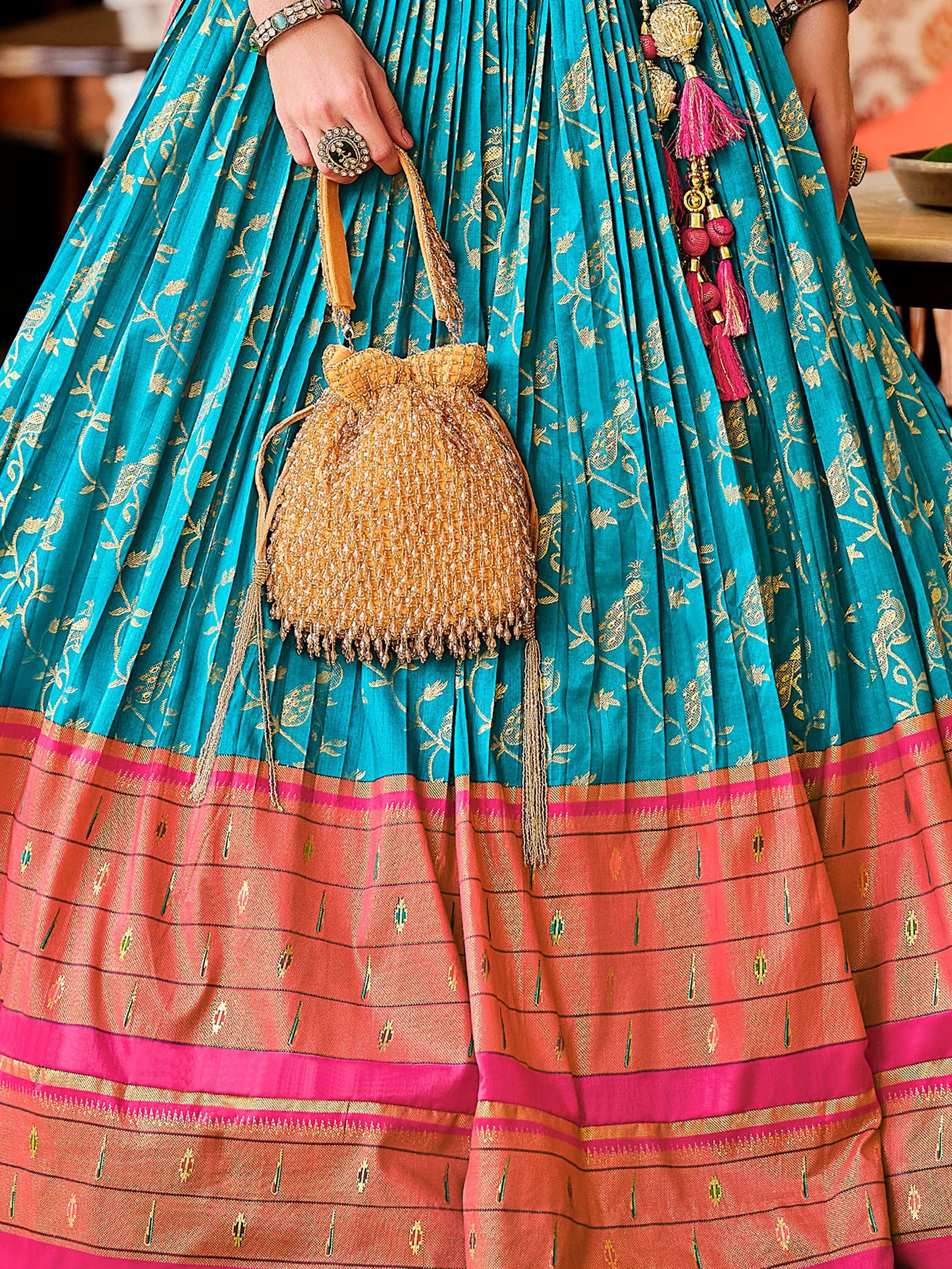 Turquoise and coral ethnic lehenga with gold embroidery, holding beaded potli bag and tassels
