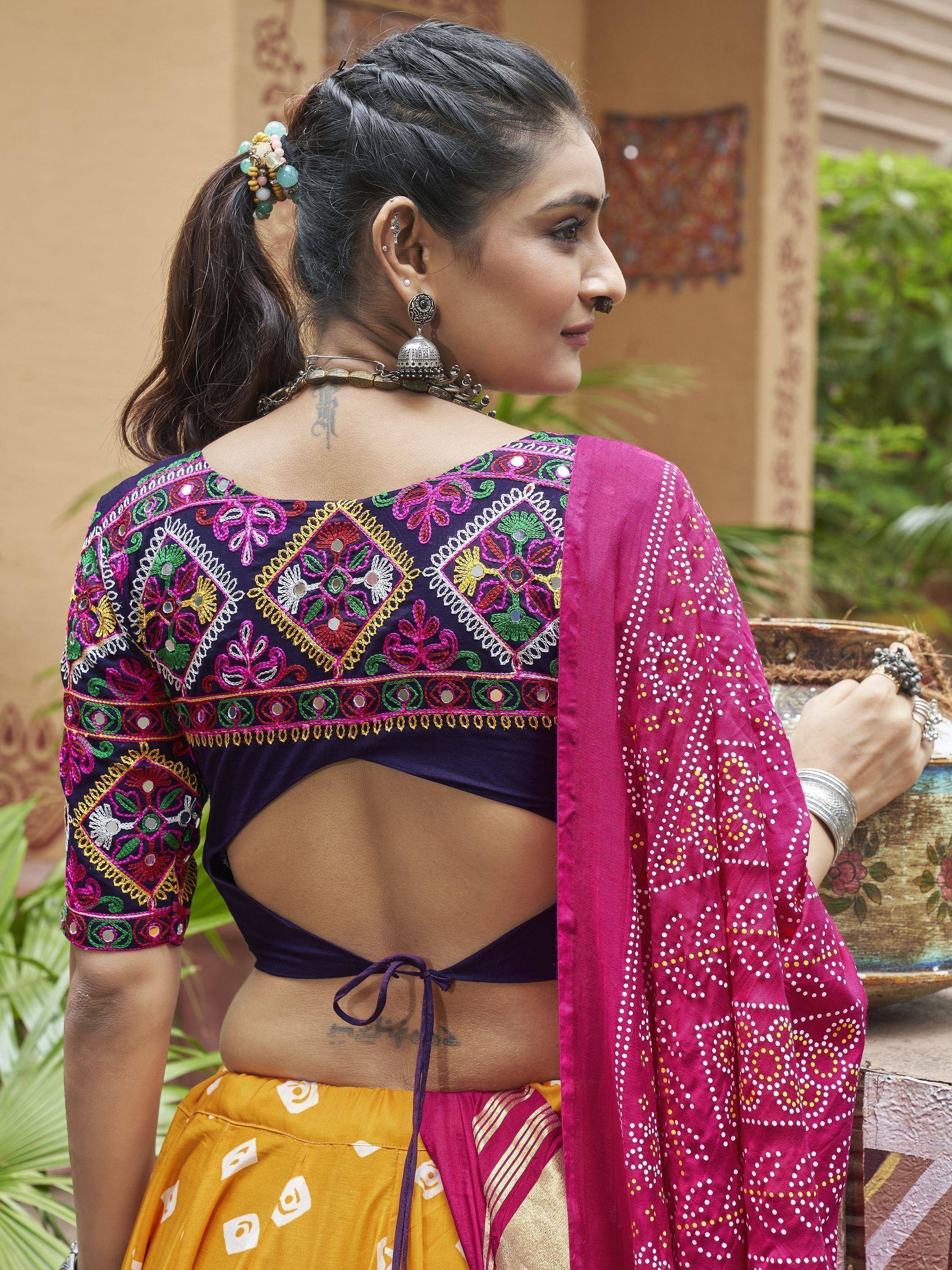 Woman in colorful embroidered ethnic blouse with mirror work, paired with yellow skirt and pink dupatta, showcasing traditional Indian fashion.