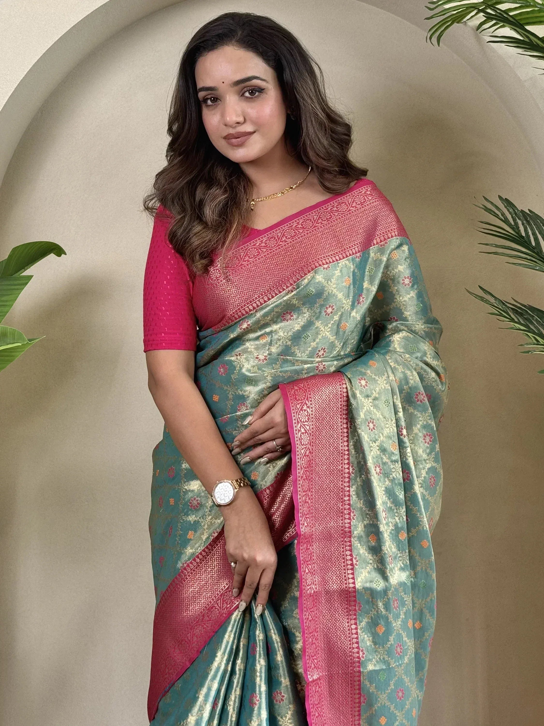 Woman in teal and pink floral saree with gold embroidery, styled with matching blouse for ethnic wear.