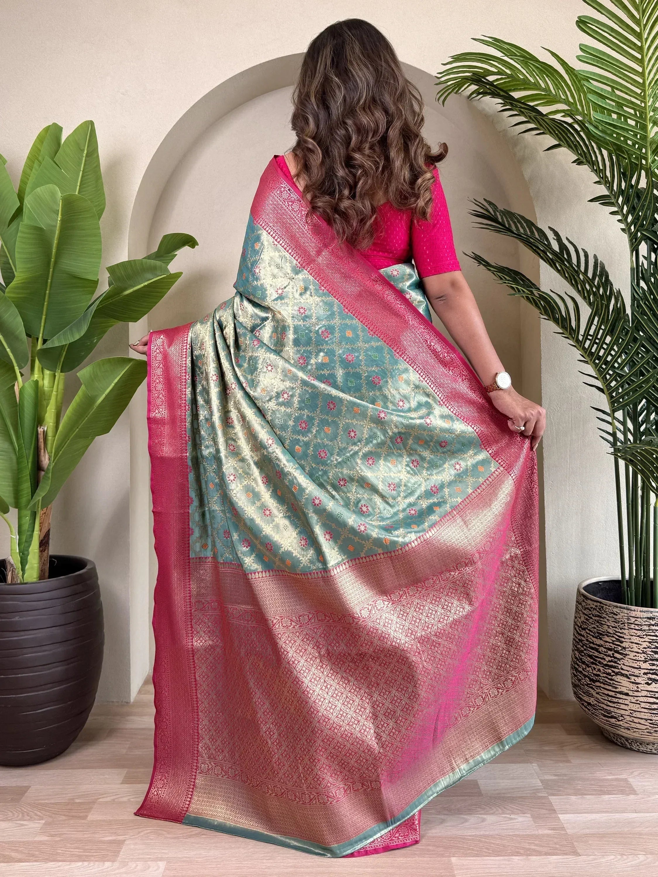 Woman wearing teal and pink designer saree with gold floral patterns, styled with matching blouse for ethnic occasions
