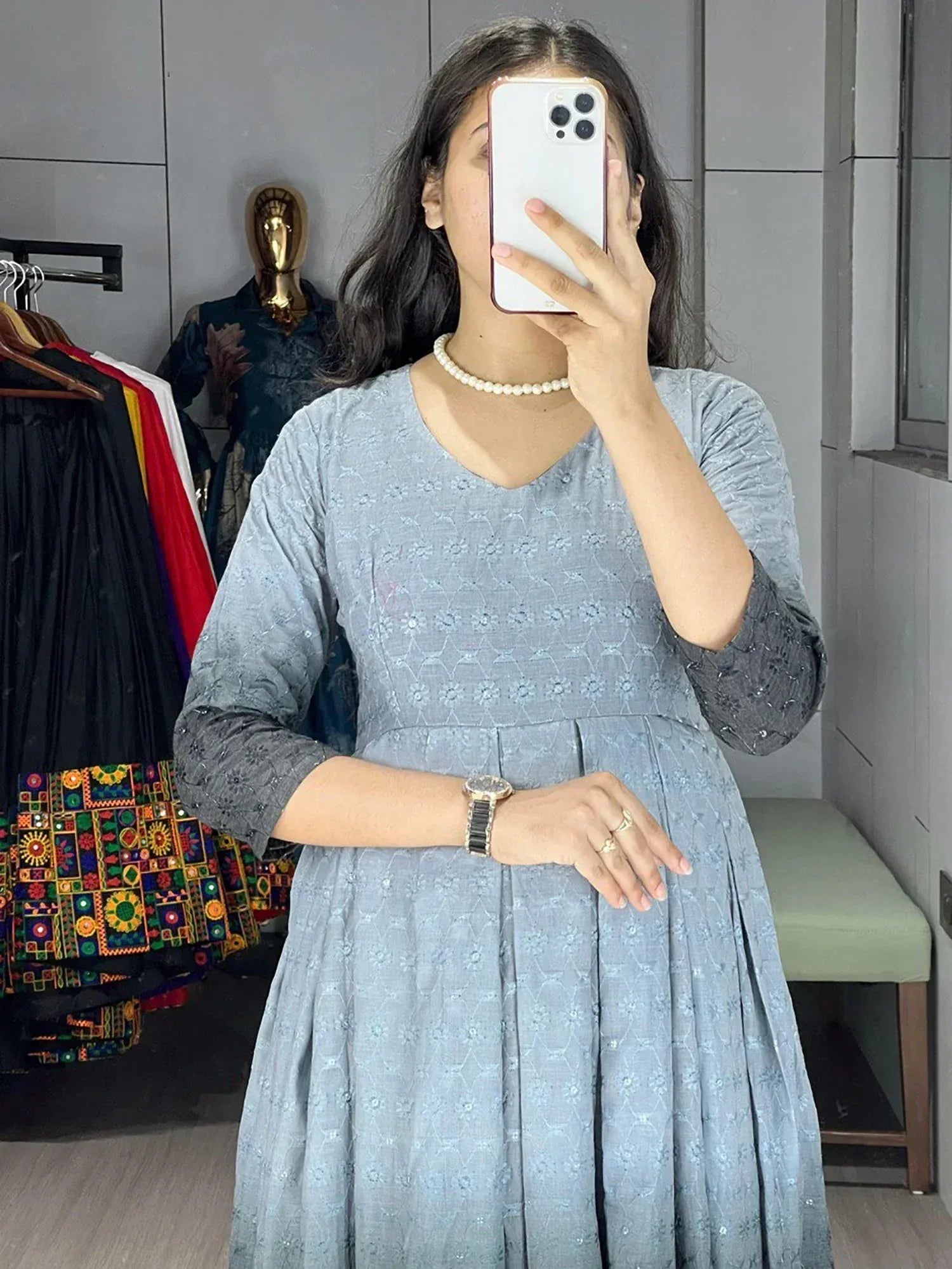 Woman in light blue embroidered ethnic gown with pearl necklace, mirror selfie in boutique