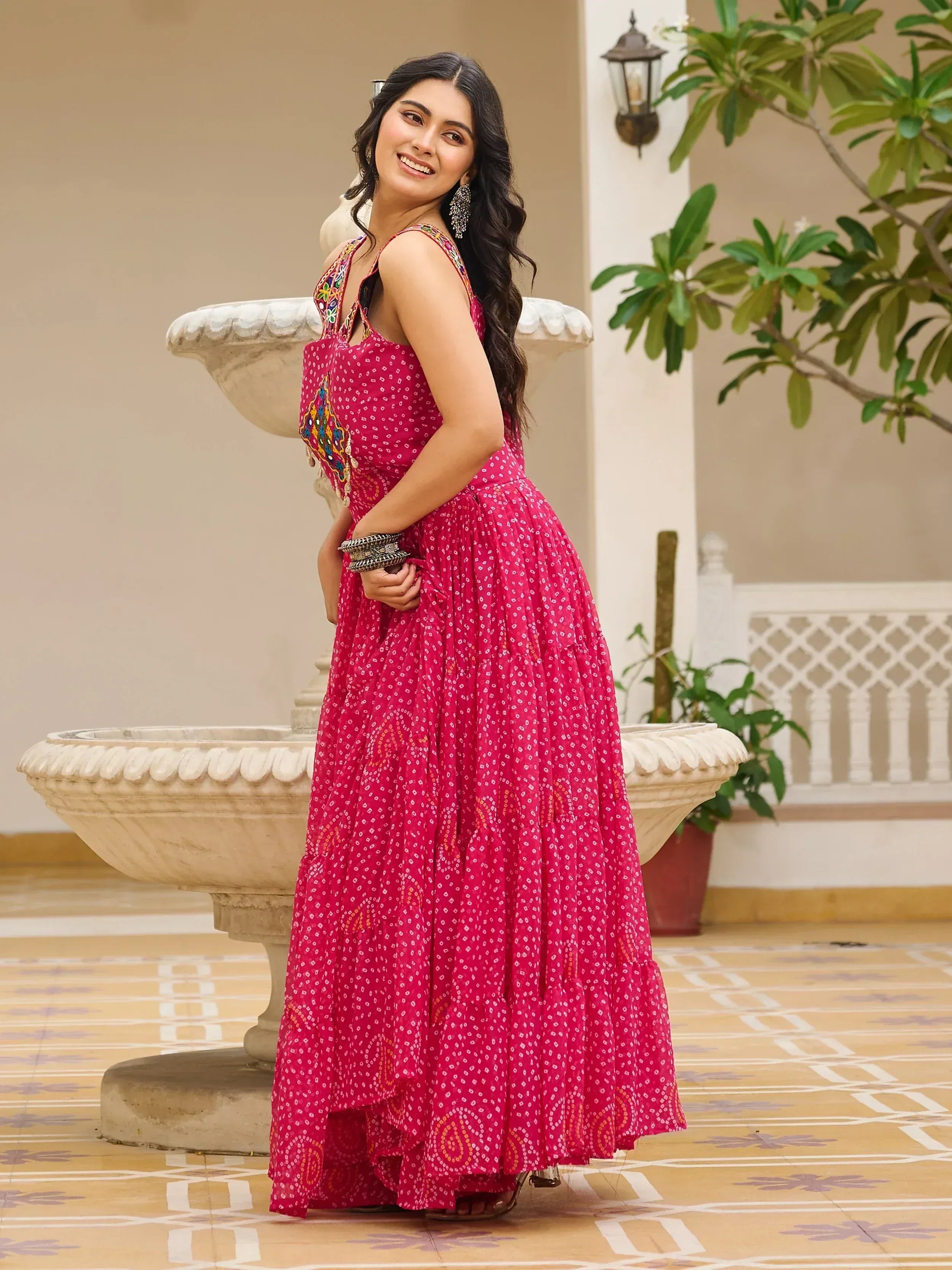 Woman in vibrant pink ethnic gown with mirror work, perfect for Indian occasions and festive wear.