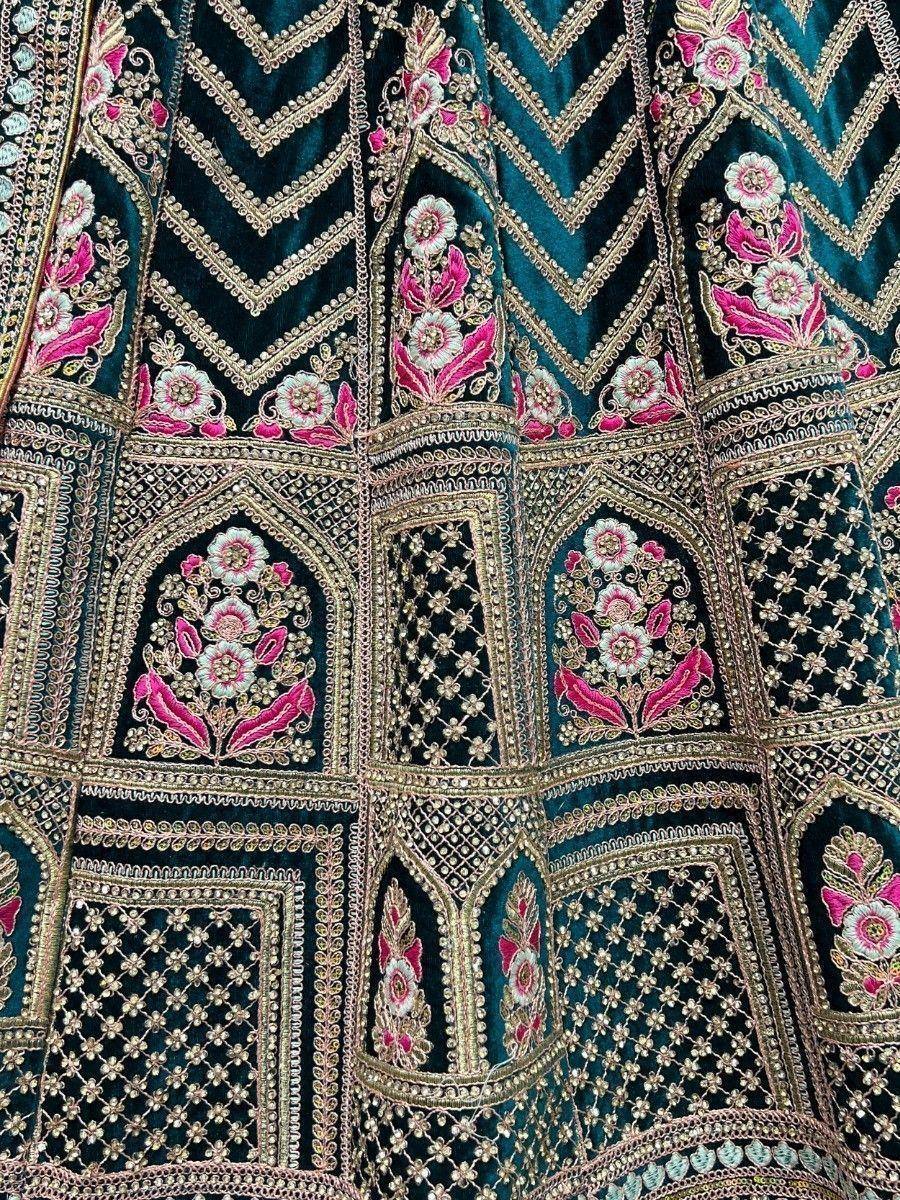 Teal velvet lehenga with pink floral embroidery and gold zari work, perfect for Indian weddings and festive occasions.