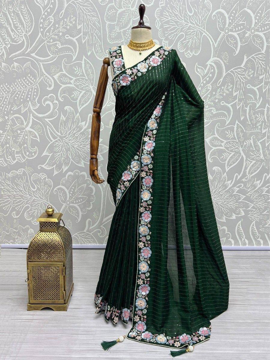 Emerald green embroidered saree with floral border, displayed on mannequin with gold jewelry and lantern decor