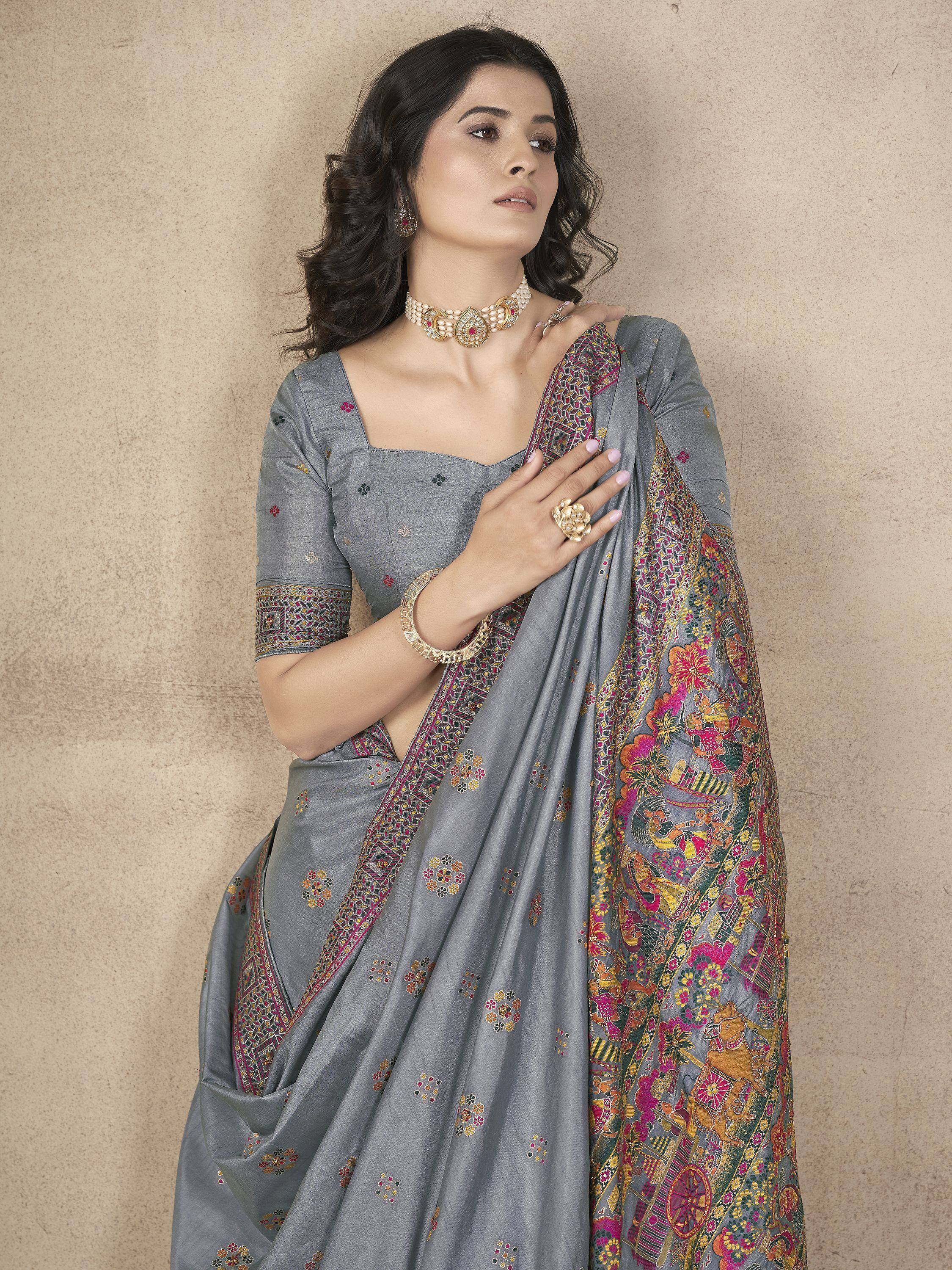 Grey embroidered saree with colorful floral and folk art border, paired with matching blouse and gold jewelry