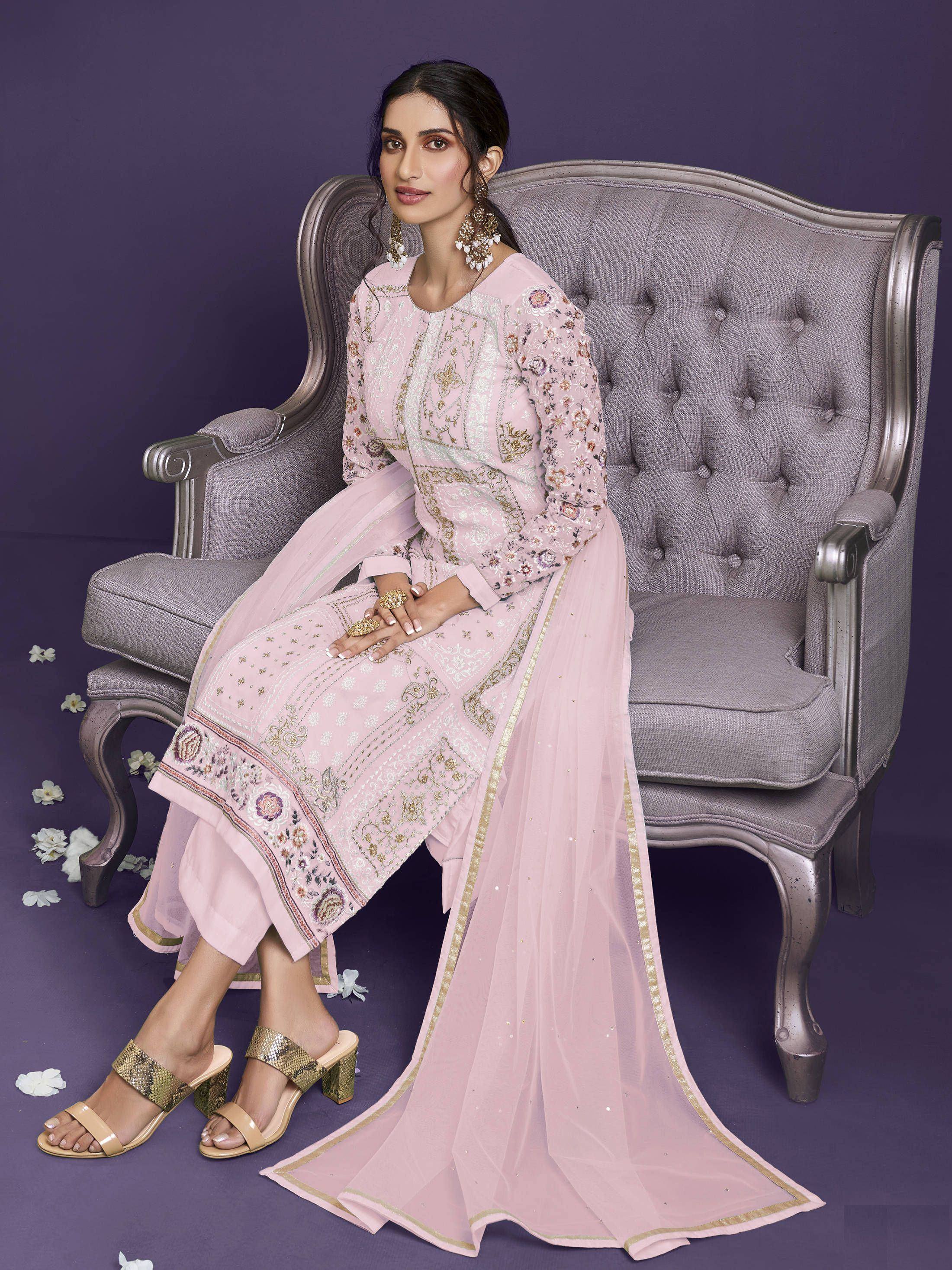 Woman in light pink embroidered salwar kameez with dupatta, sitting on an elegant sofa