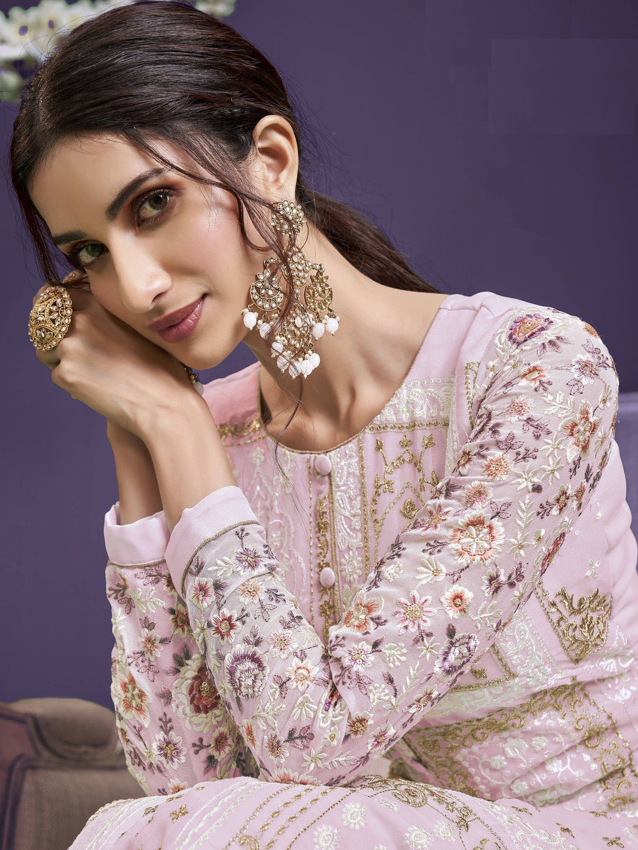 Woman in pastel pink floral embroidered ethnic gown with heavy earrings, posing elegantly
