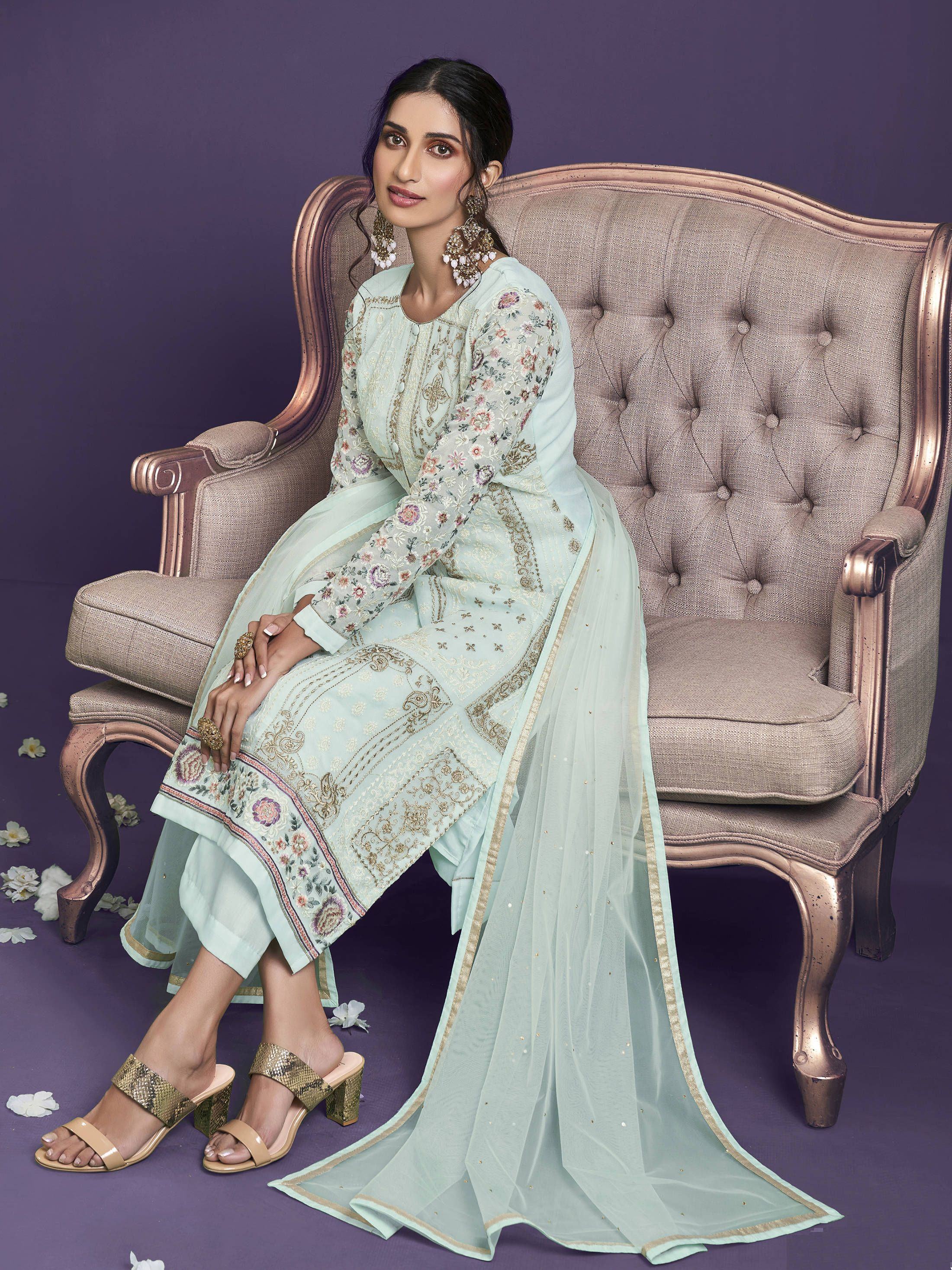 Woman wearing light blue embroidered salwar kameez with dupatta, seated on elegant sofa