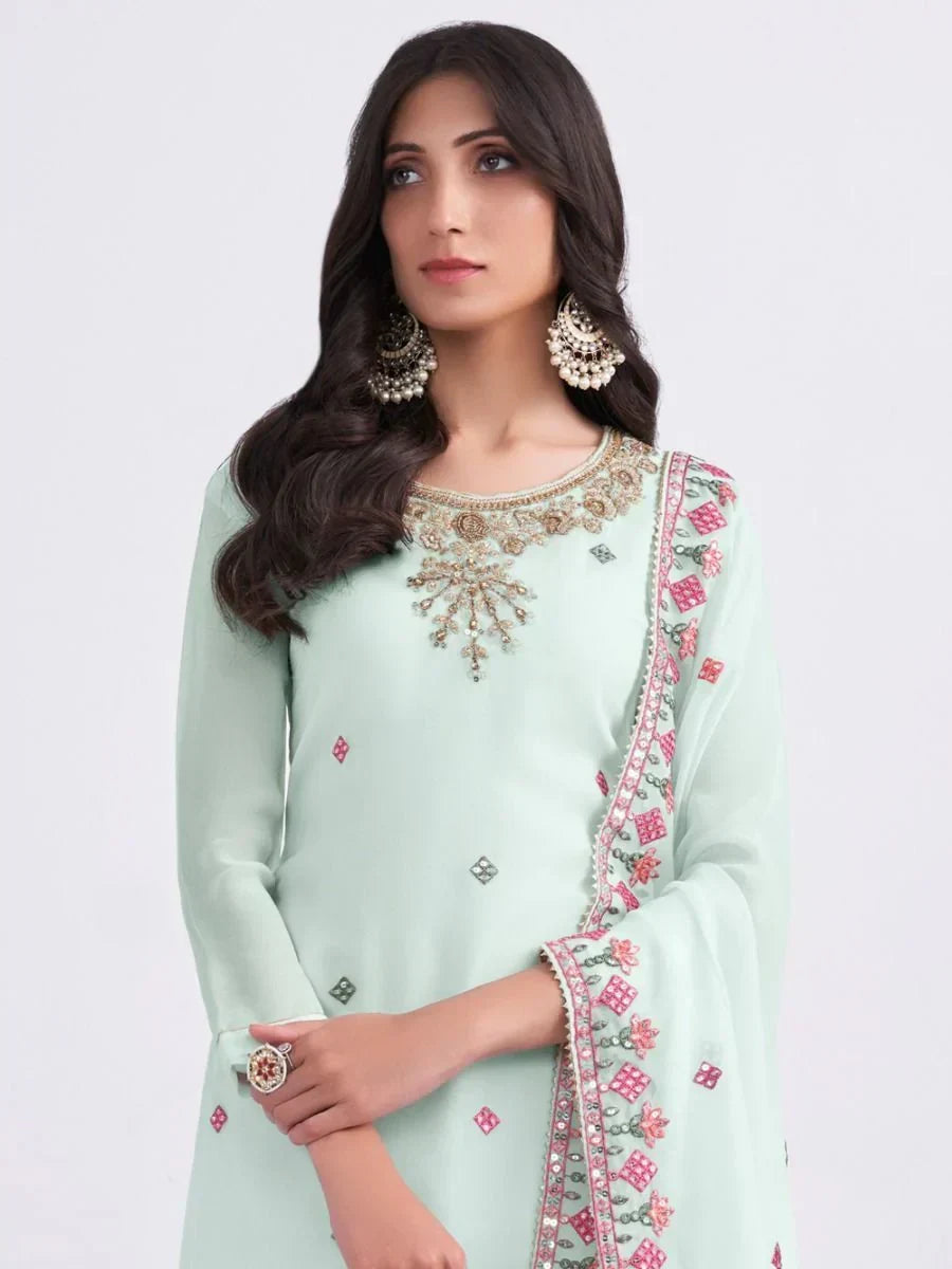 Woman in pastel green embroidered salwar kameez with matching dupatta and statement earrings