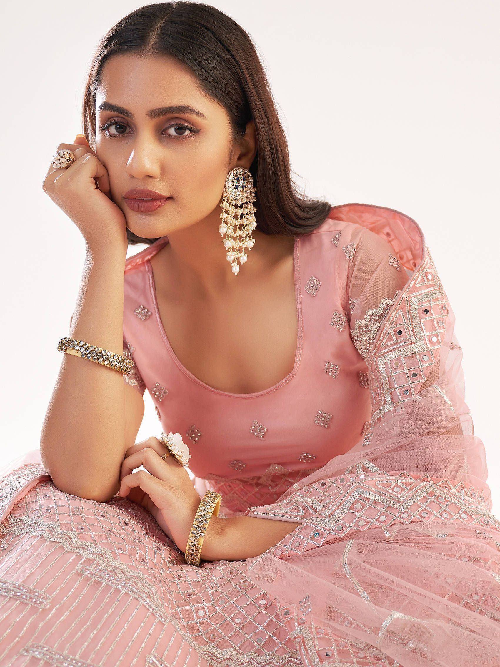 Pink embroidered lehenga choli with mirror work, paired with statement earrings and bangles for Indian ethnic wear.