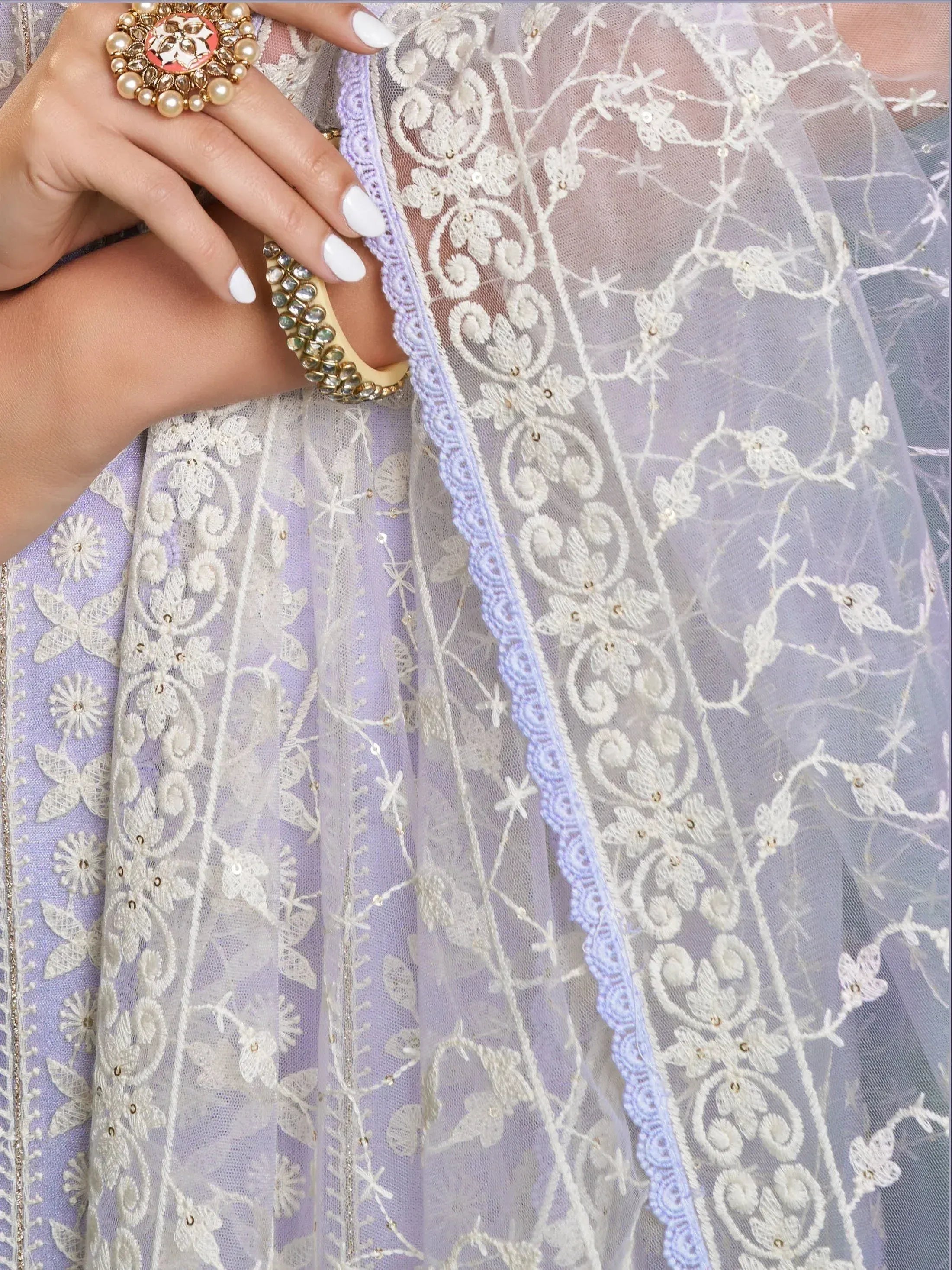 Lavender ethnic gown with white floral embroidery and lace detailing, paired with traditional jewelry.