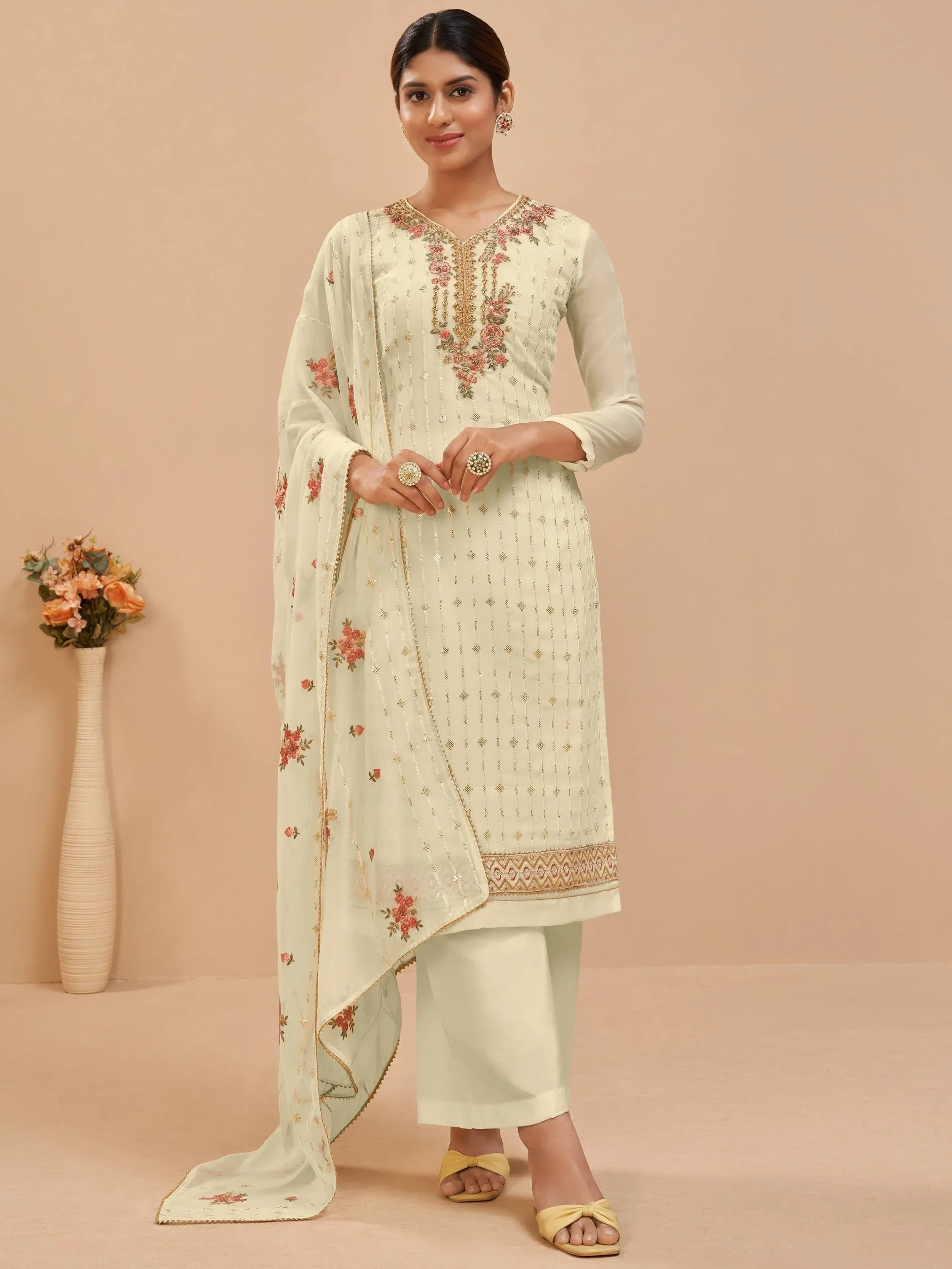 Woman in cream embroidered salwar kameez with matching dupatta, standing indoors