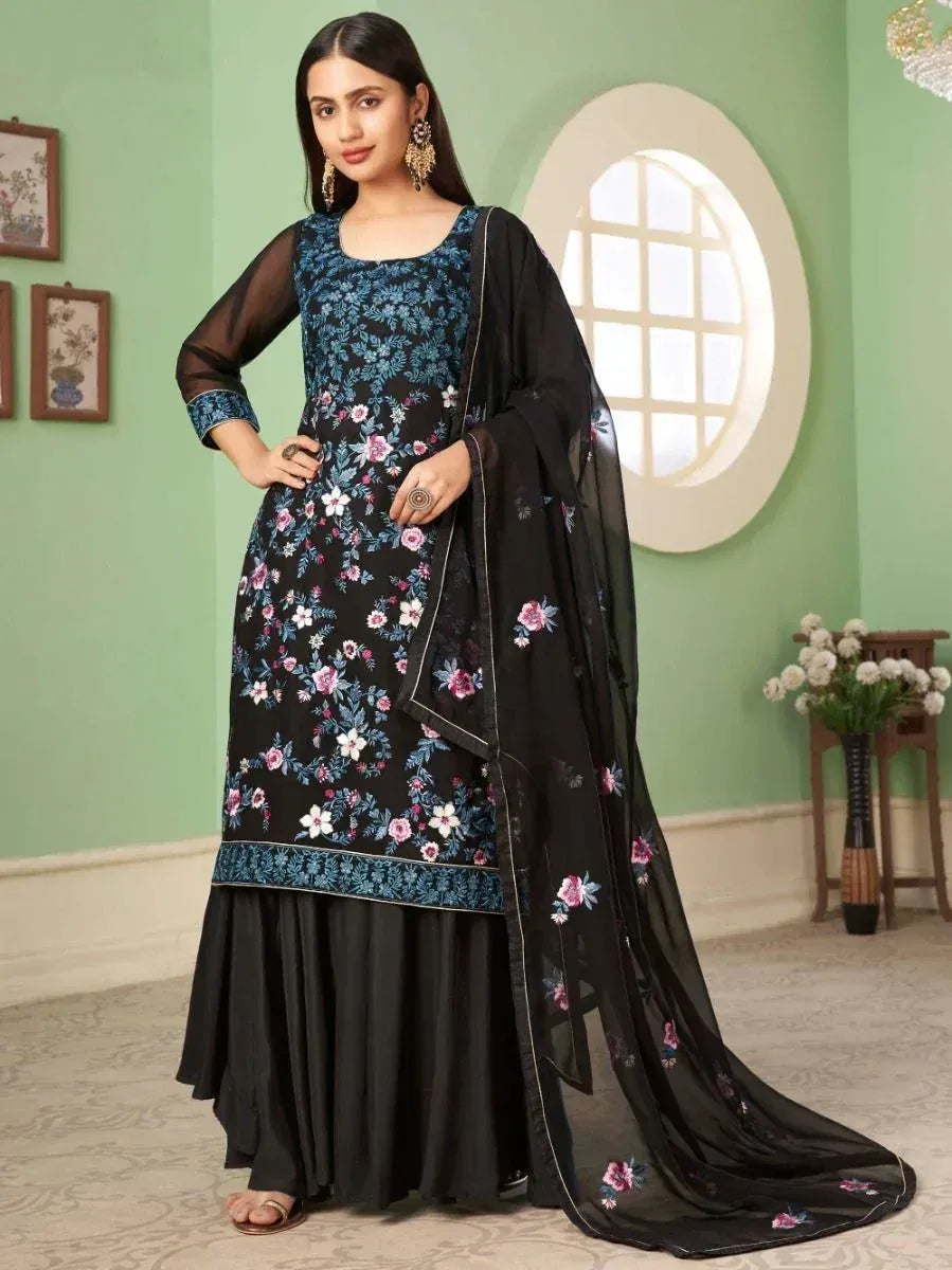 Woman in black floral embroidered salwar kameez with matching dupatta, standing indoors